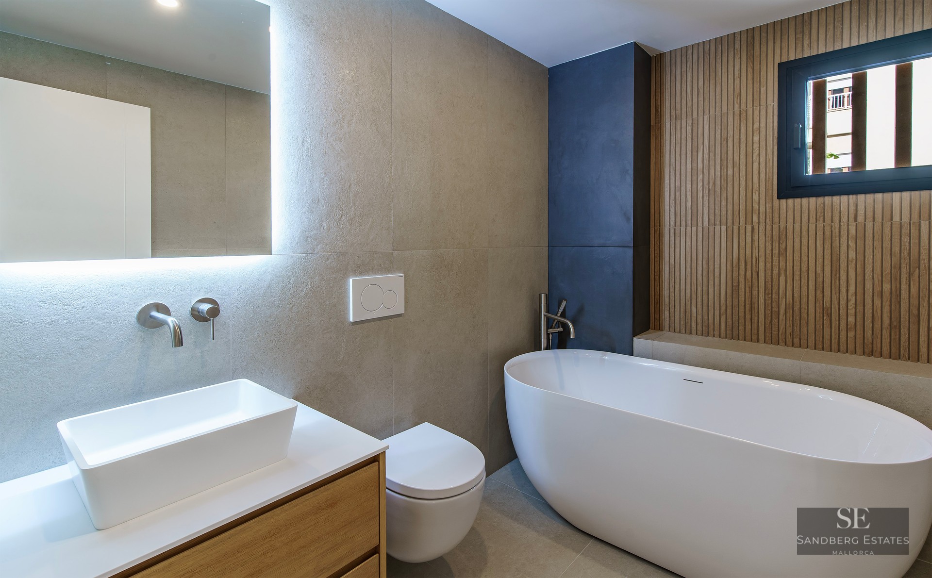 Salle de bain moderne avec baignoire îlot, vasque sur meuble en bois et miroir rétroéclairé.