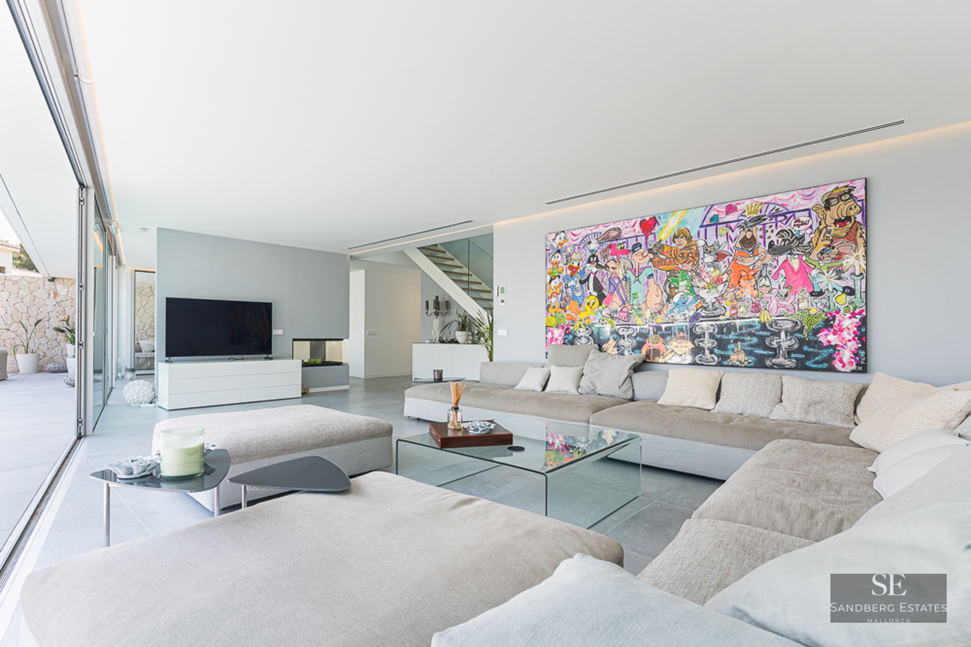 Modern living room with large beige sofa, glass table, and a massive colorful cartoon painting on a white wall.