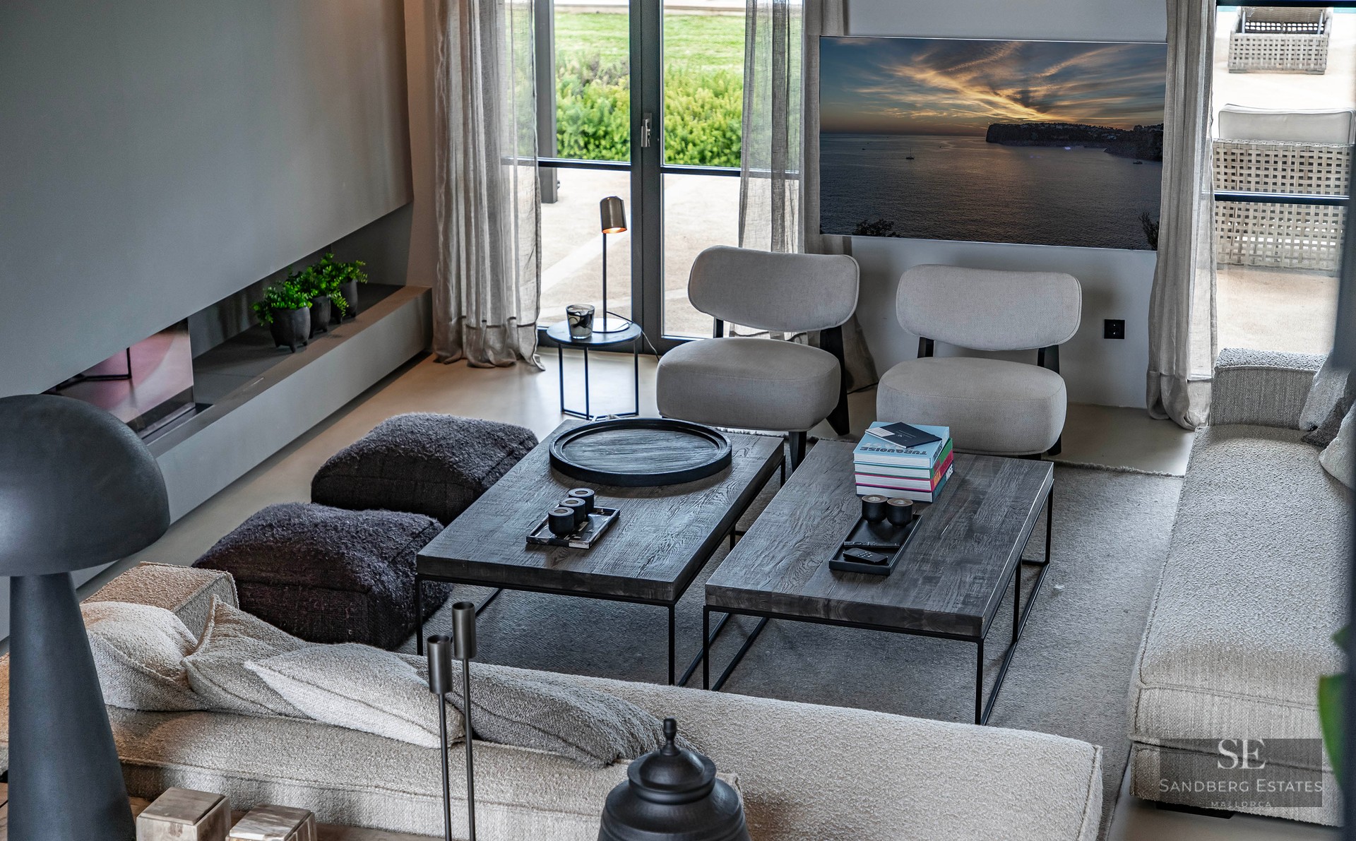 High-angle view of a luxury living room with grey seating, dark wood coffee tables, linear fireplace, and garden window.