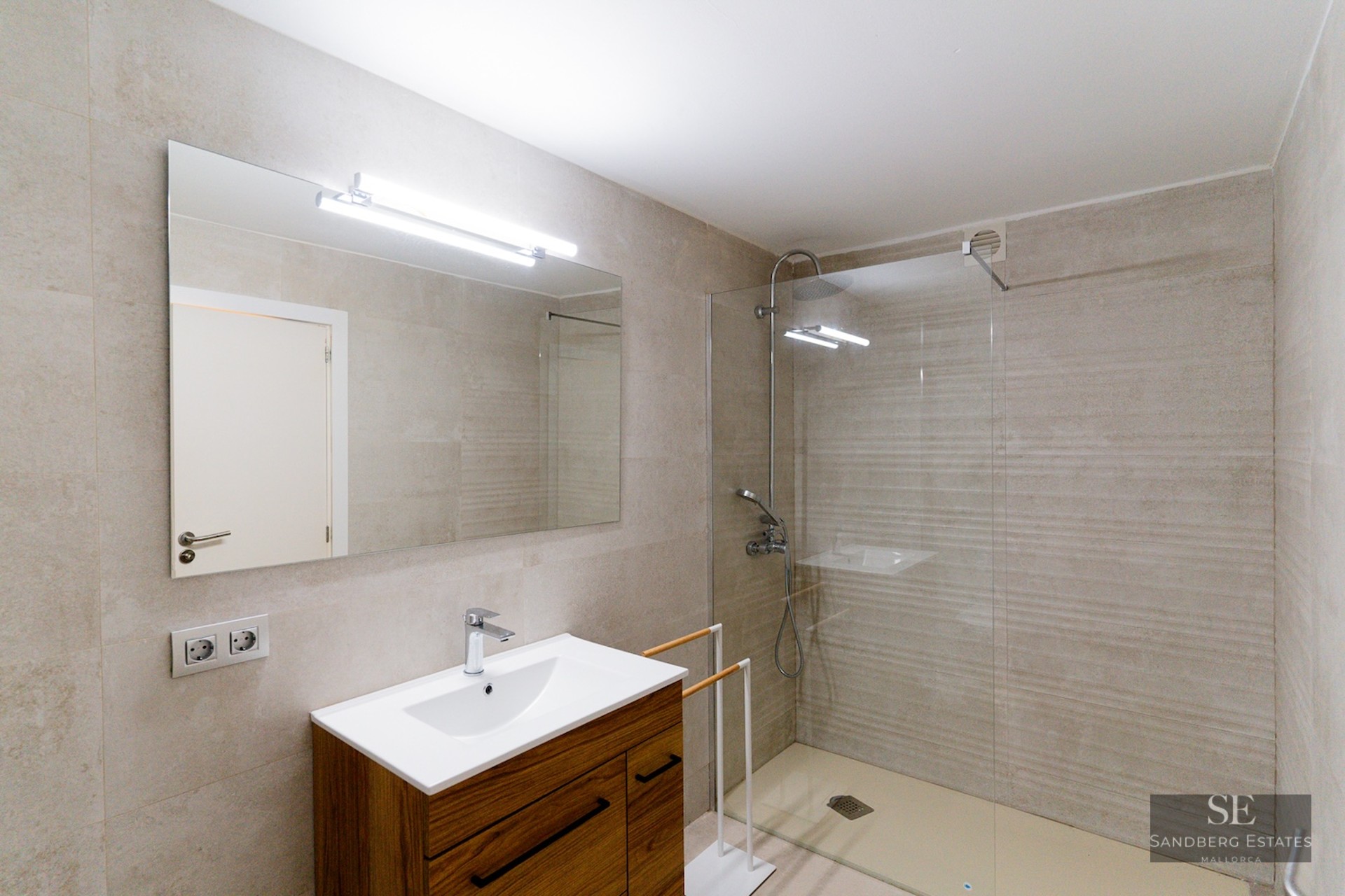 Contemporary bathroom featuring a walk-in glass shower, stone tiles, and a wooden vanity with a large mirror.