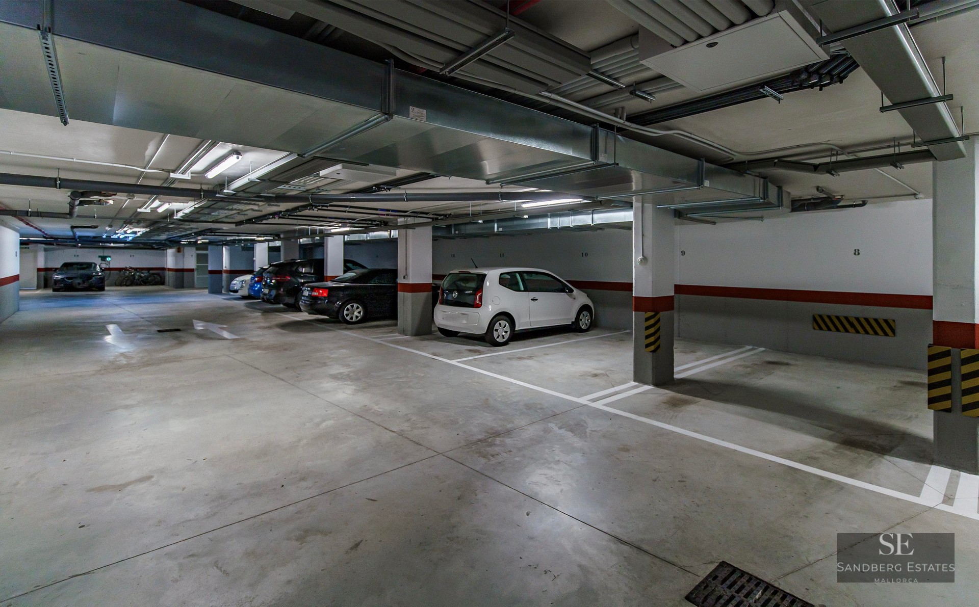 Well-lit underground parking garage with numbered stalls, parked cars, and overhead ventilation ducts.
