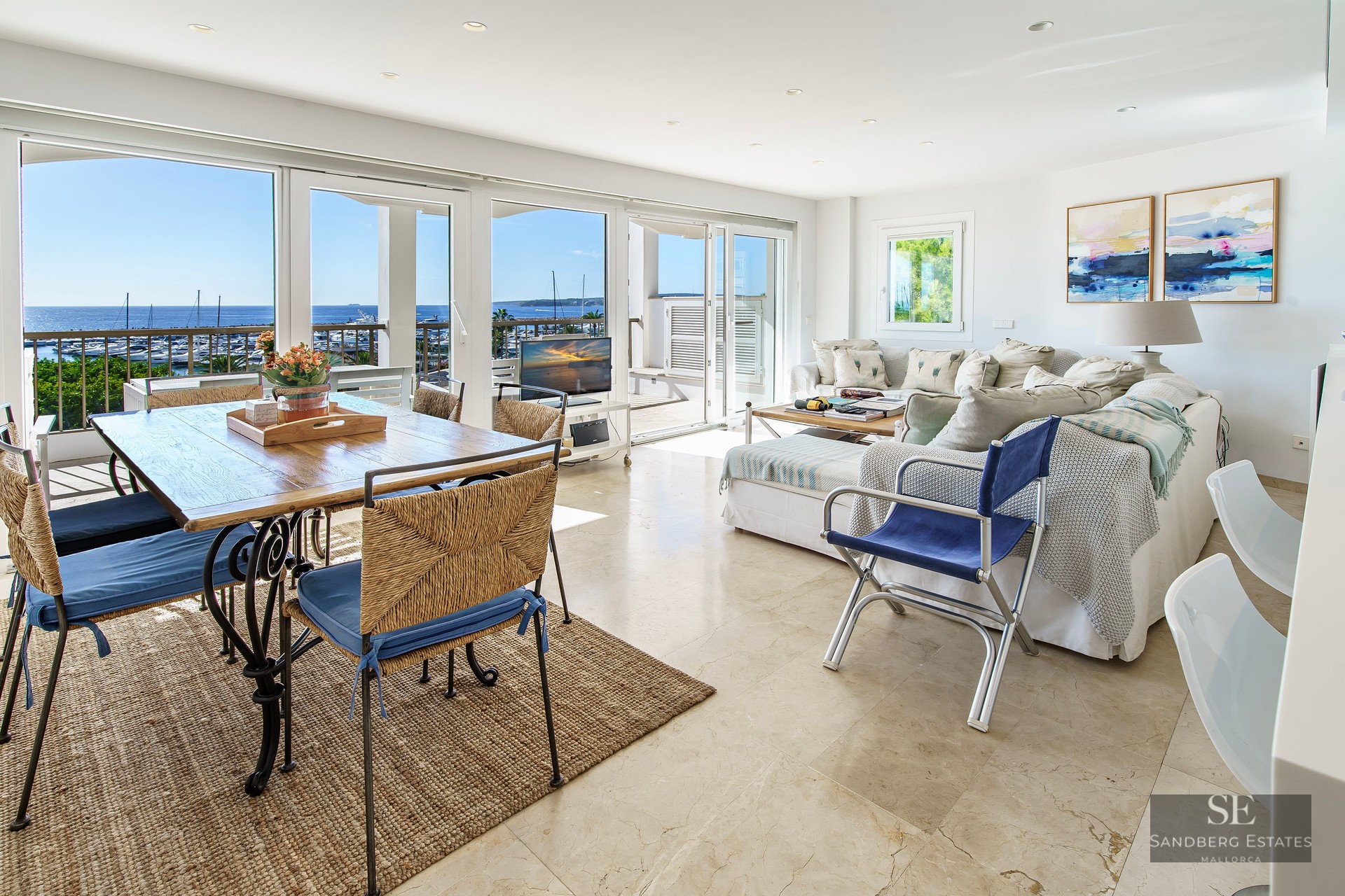 Open-plan living room with marble floors and large windows overlooking a marina and sea.