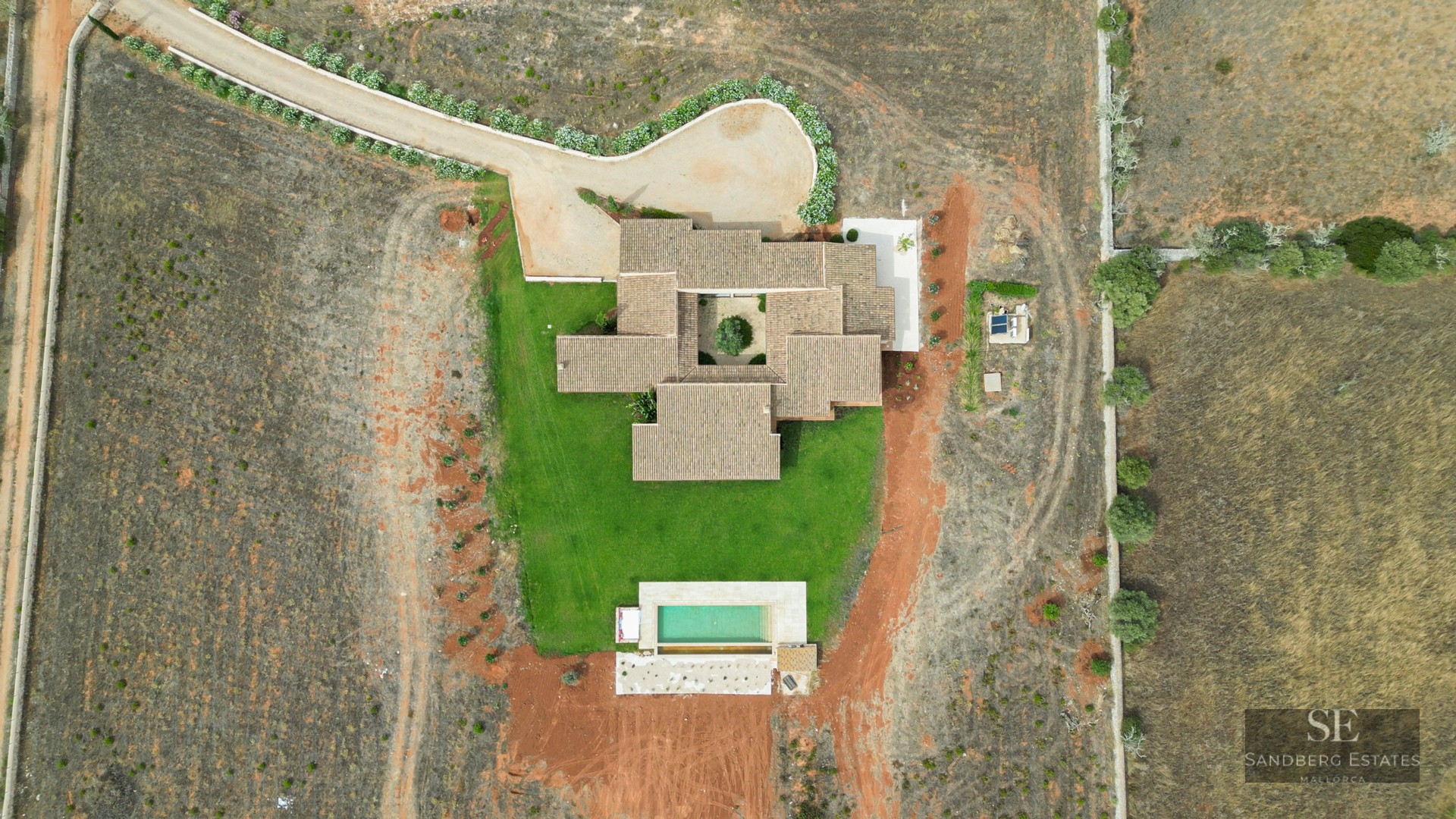 Top-down drone view of a tiled-roof villa with a central interior courtyard, lawn, and rectangular swimming pool.