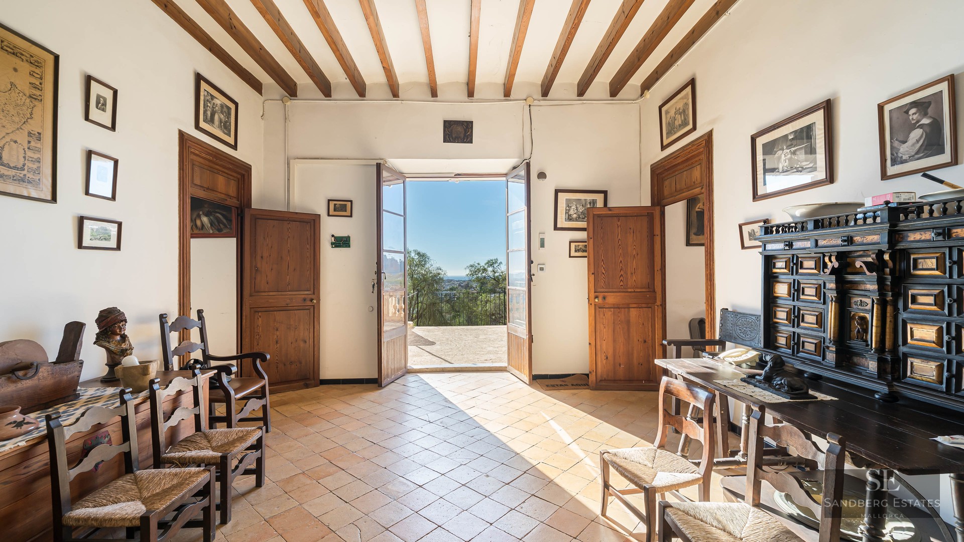 Traditional hallway with wooden beams, terracotta floors, and open doors leading to a sunny terrace.