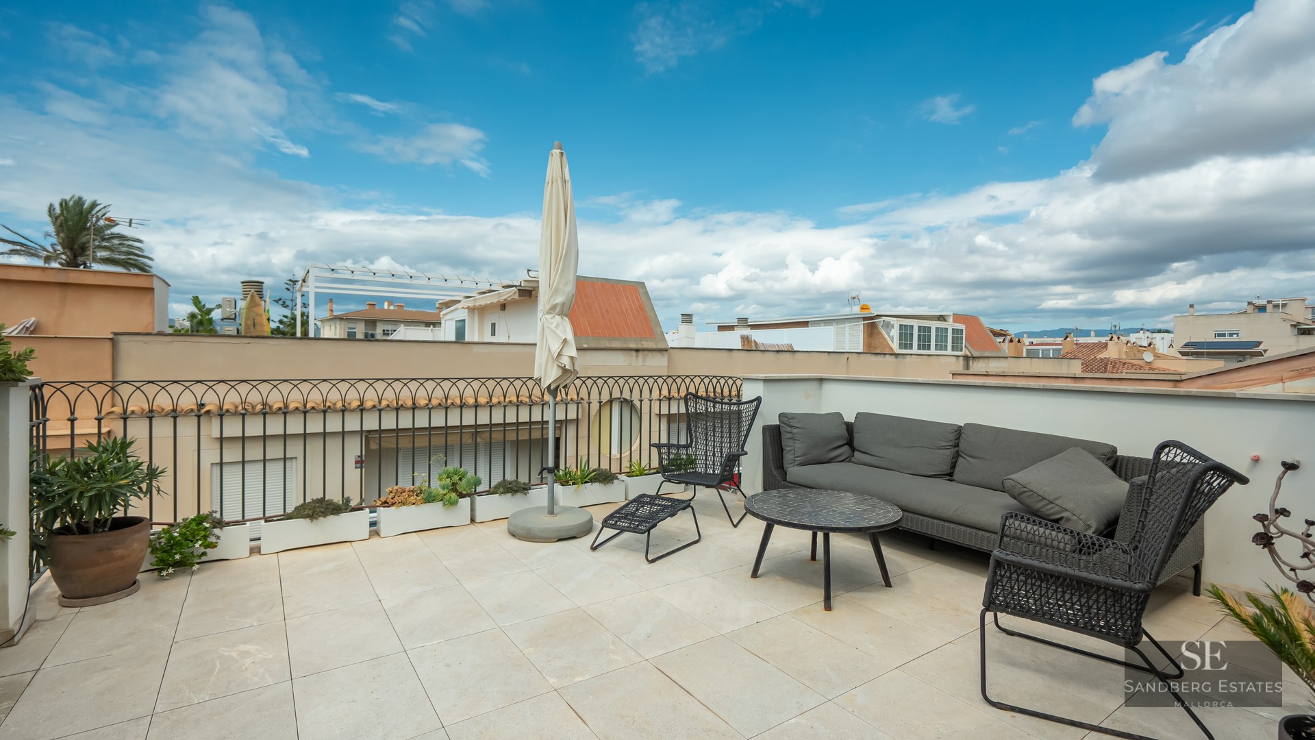 Rooftop terrace with grey sofa, black chairs, and a white umbrella under a blue sky.