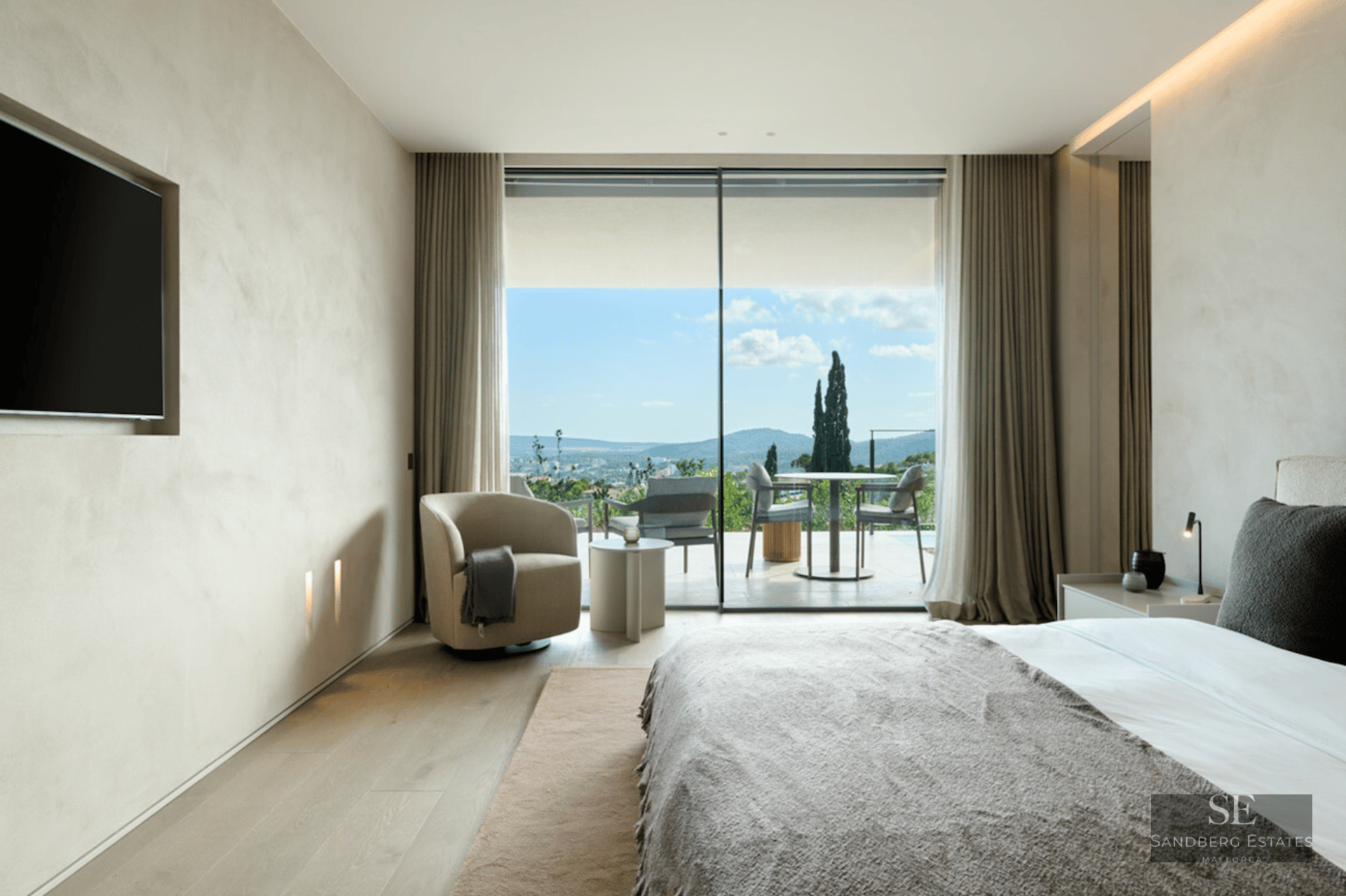 Luxury bedroom with floor-to-ceiling windows showing a scenic mountain view and a furnished terrace.