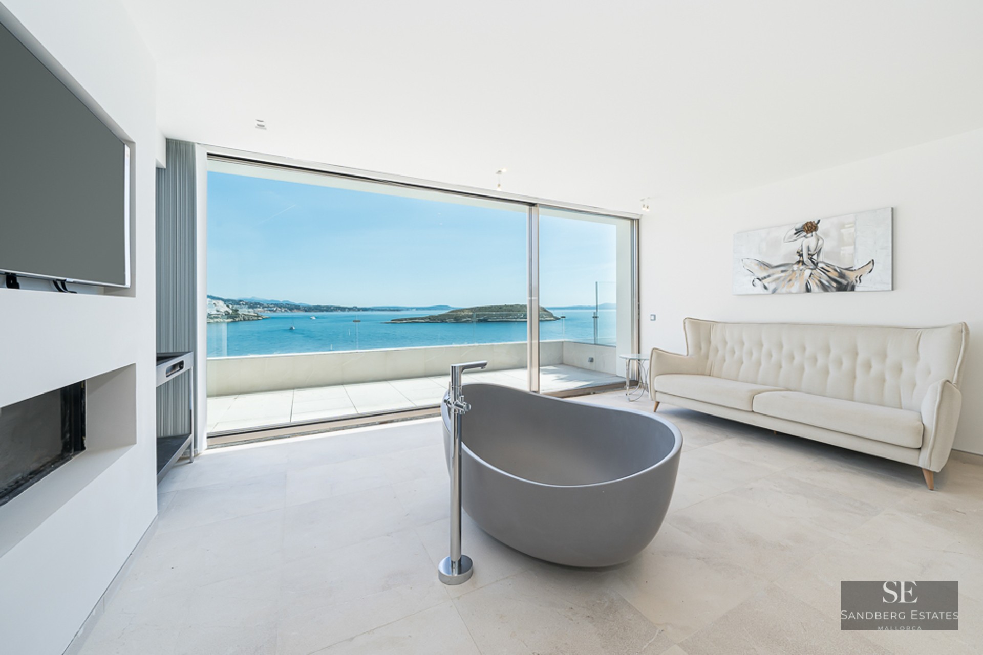 Modern master bathroom featuring a freestanding grey tub, cream sofa, and floor-to-ceiling windows overlooking the ocean.