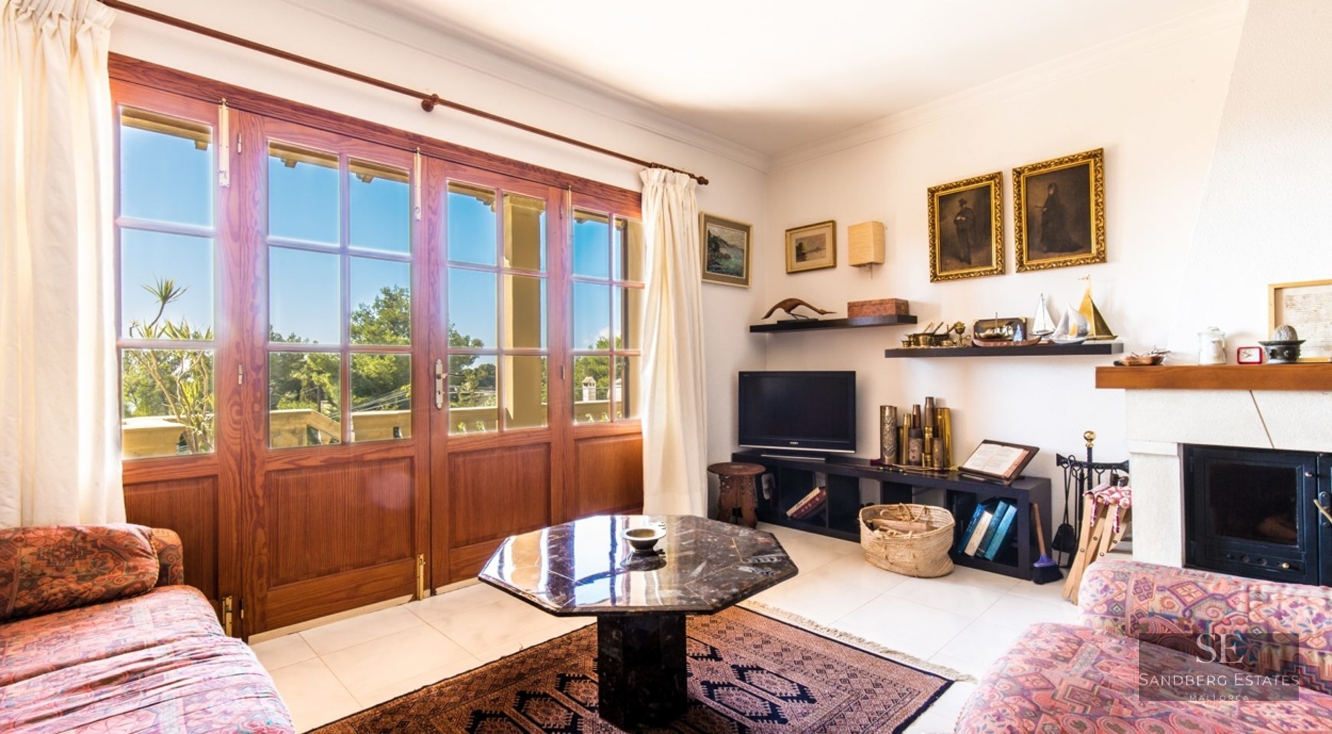 Living room with patterned sofas, hexagonal marble coffee table, fireplace, and large wooden doors leading to a terrace.