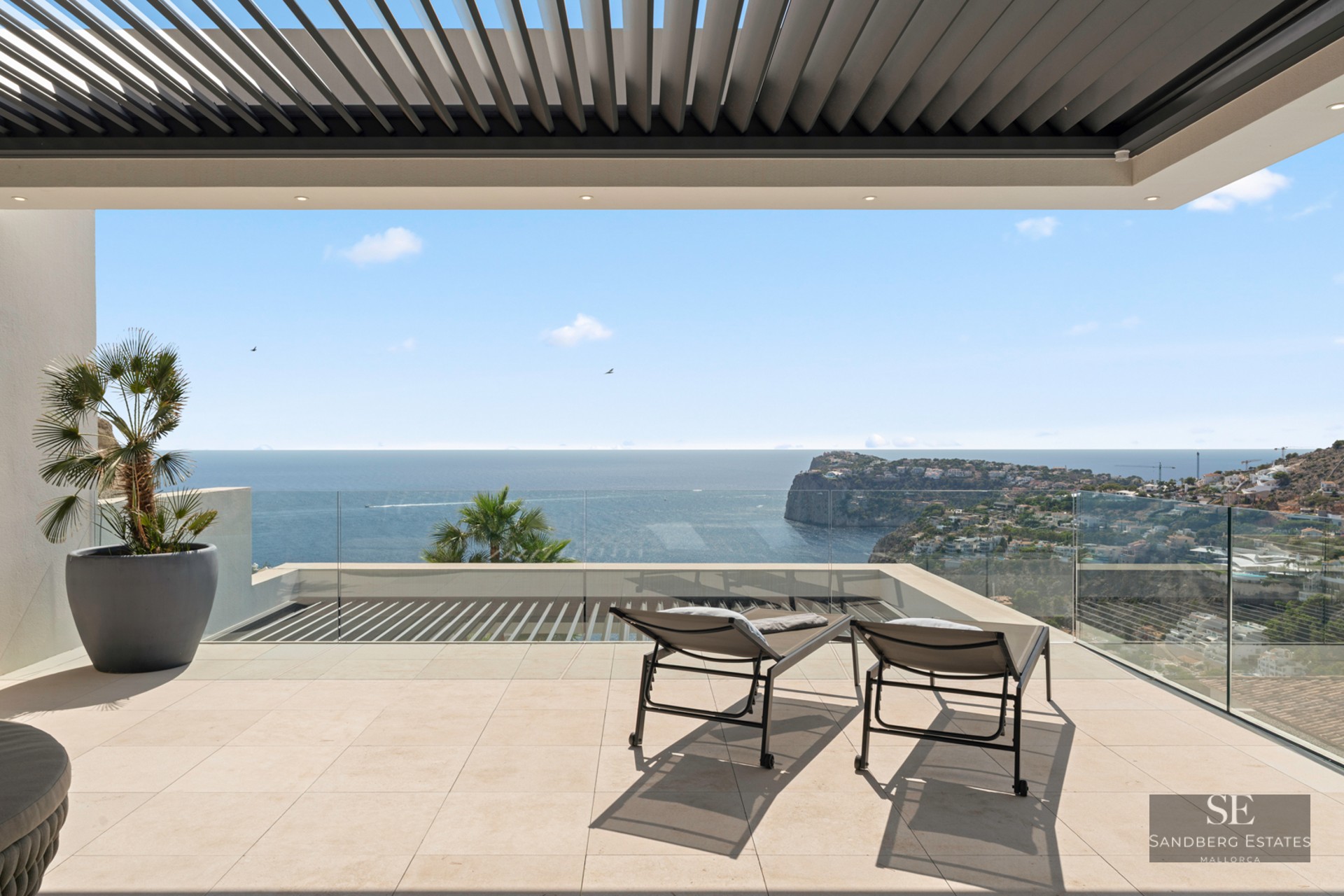 Modern terrace with glass railings, two sun loungers, and a wide view of the ocean and coastal cliffs.