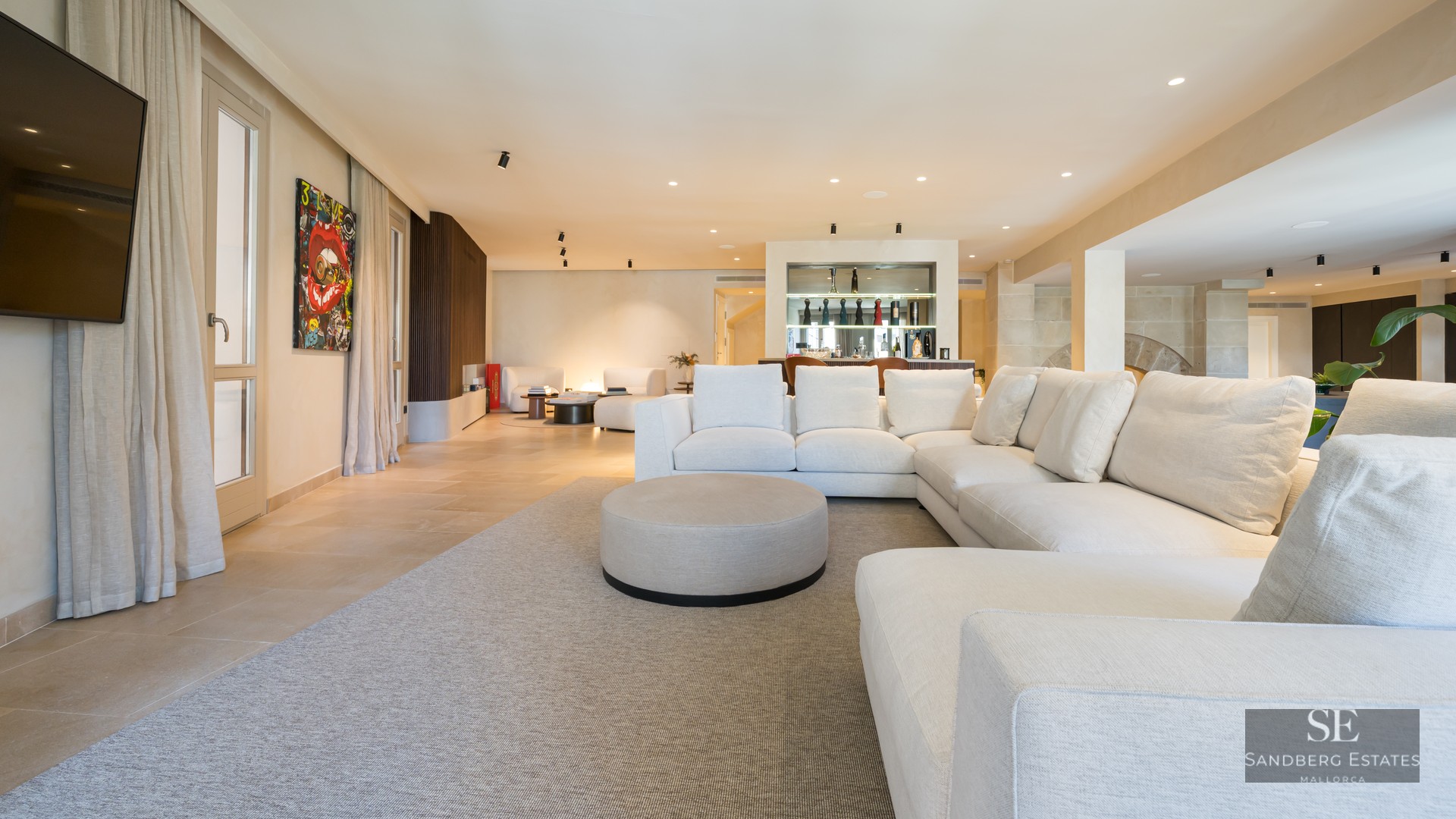 Large white sectional sofa in a spacious, modern living room with stone floors and a built-in bar area.