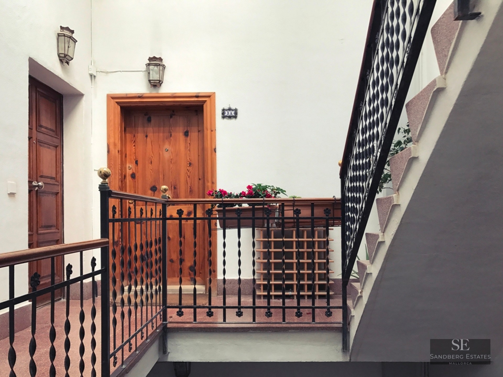 Bright building landing featuring solid wood doors, wrought iron railings, and white walls.