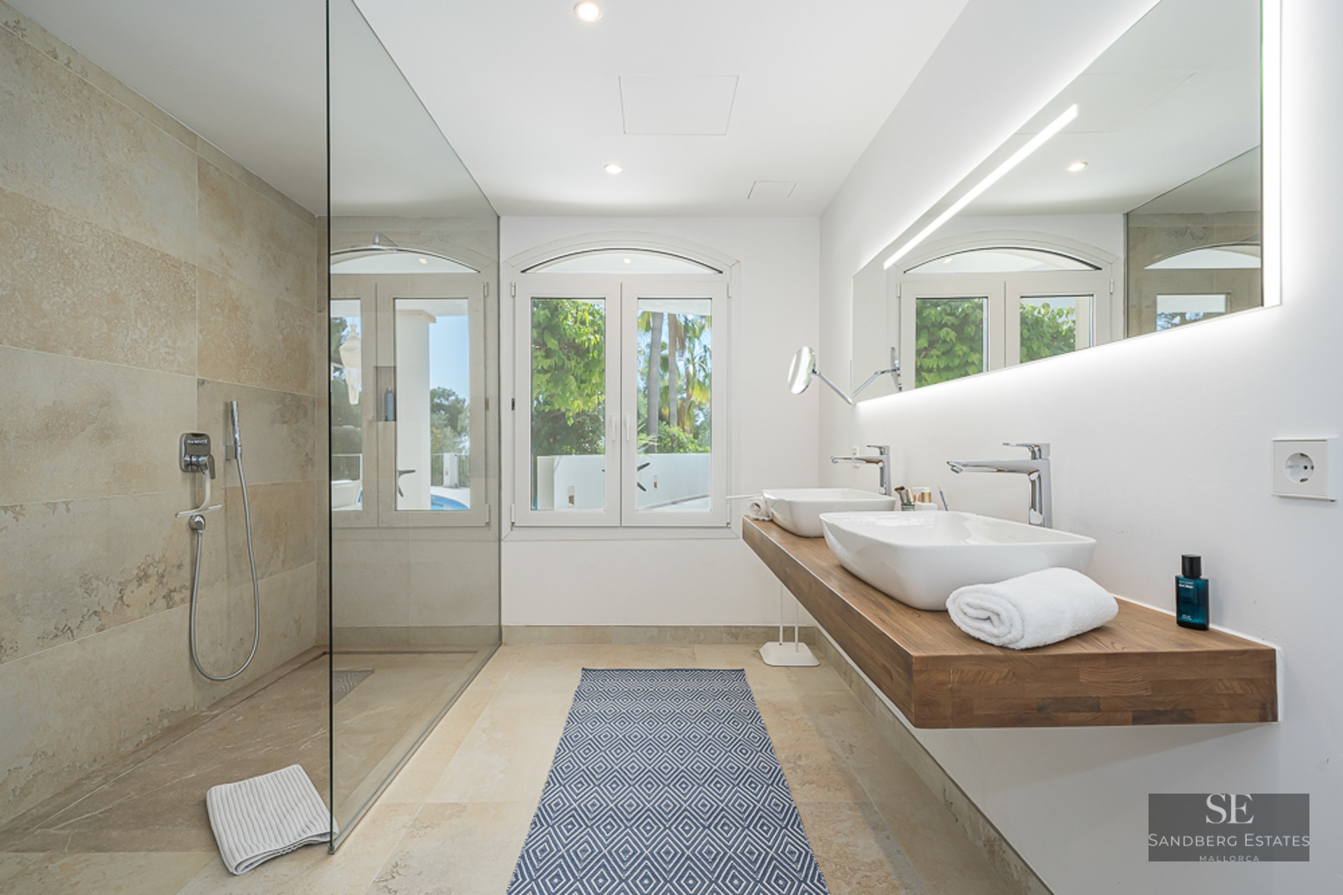 Salle de bain moderne avec une grande douche vitrée, double vasque sur plan en bois et vue sur le jardin.