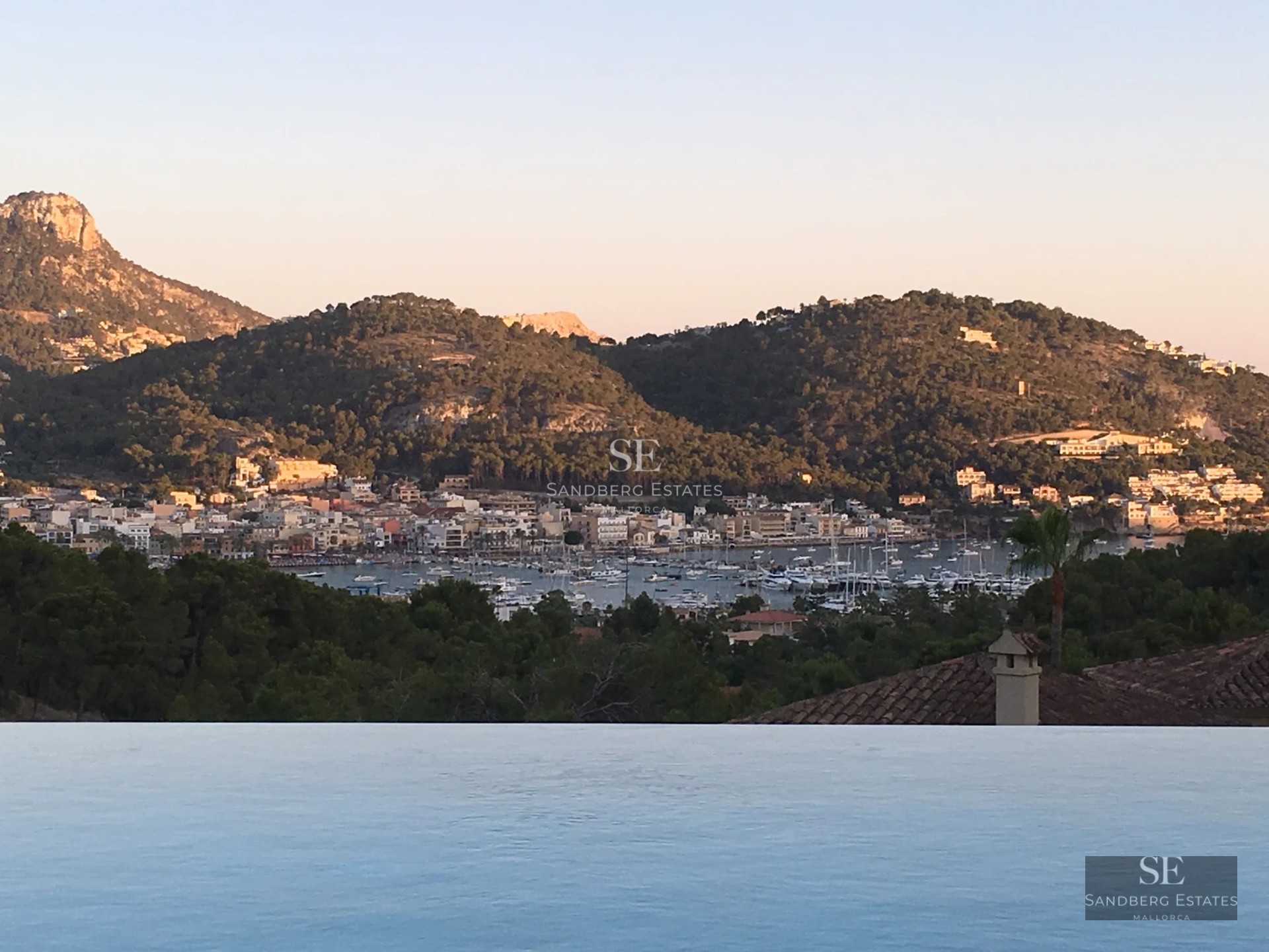 Modern terrace with sea view. Glass railing, designer outdoor furniture, and wooden flooring. Soft ambient lighting.