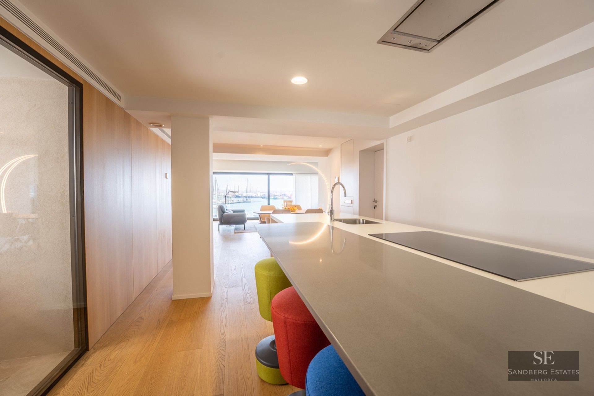Kitchen island with colorful stools looking through a living area to a marina view through large windows.