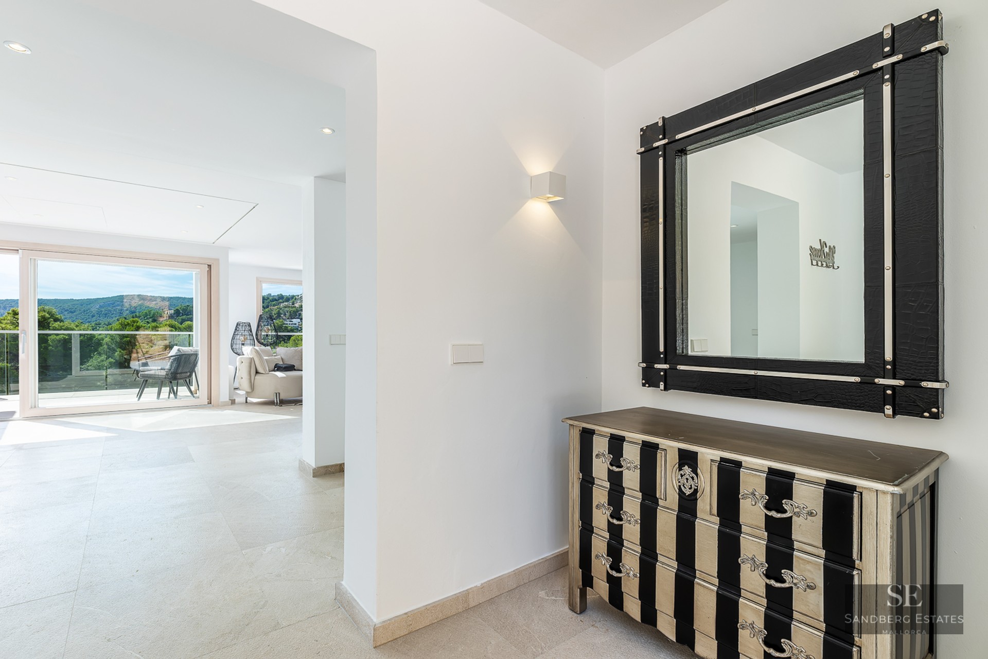 Modern entrance hall featuring a black and silver chest, large mirror, and a bright view of mountains.