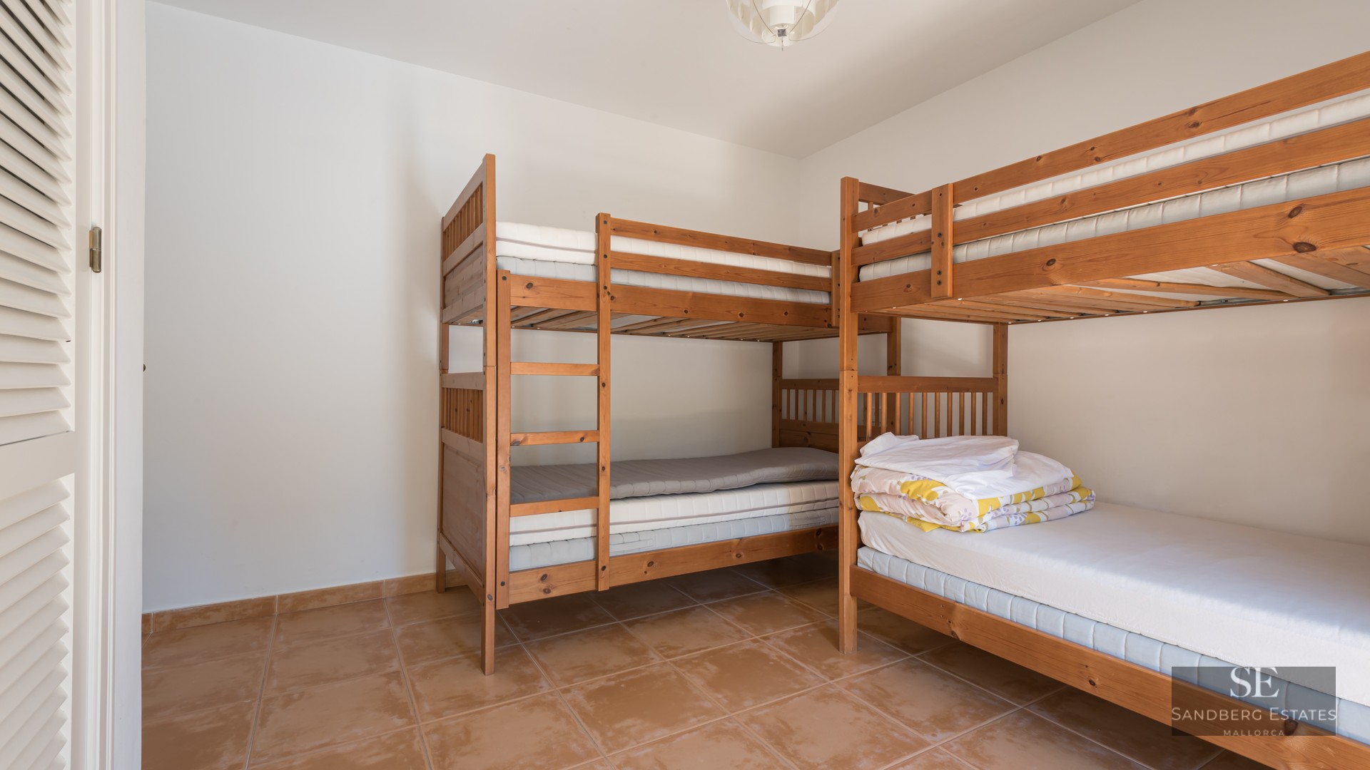 A bright bedroom with two wooden bunk beds and terracotta tiled floors.