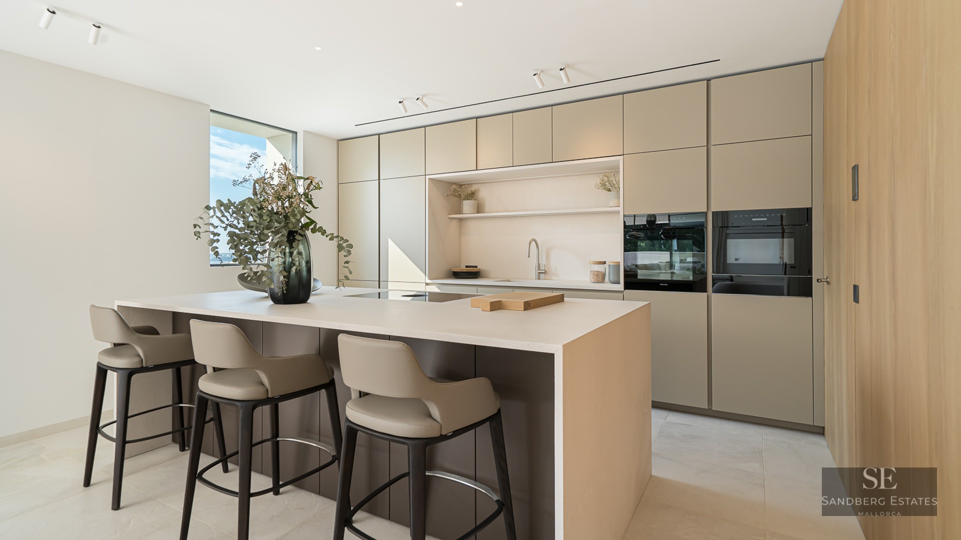 Modern minimalist kitchen featuring a large central island, designer bar stools, and sleek earth-toned cabinetry.