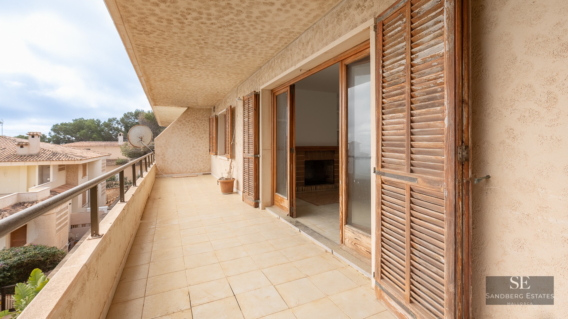 Long tiled balcony with weathered wooden shutters and glass doors leading to an indoor living area.