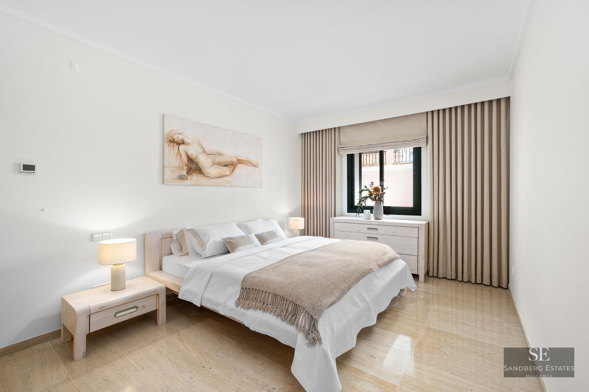 Chambre lumineuse avec lit en bois clair, sol en marbre, murs blancs et un grand tableau au-dessus du lit.