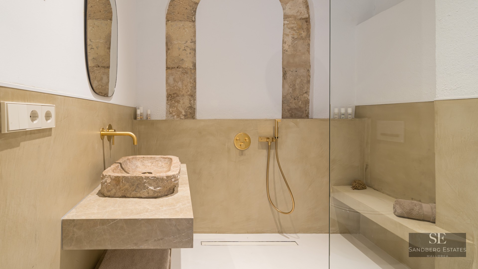 Salle de bain moderne avec une vasque en pierre brute, robinetterie dorée et douche à l'italienne vitrée.