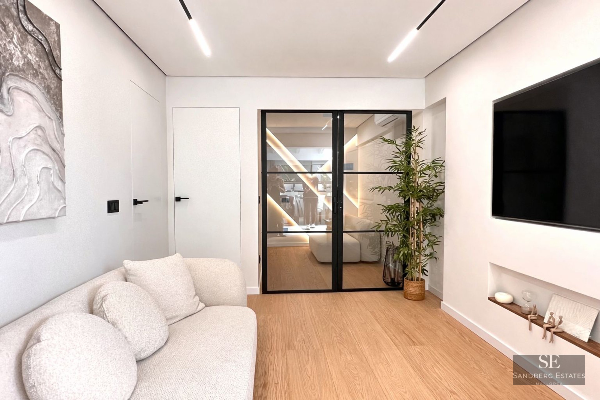 Modern living room featuring a white textured sofa, light wood floors, and black-framed glass double doors.