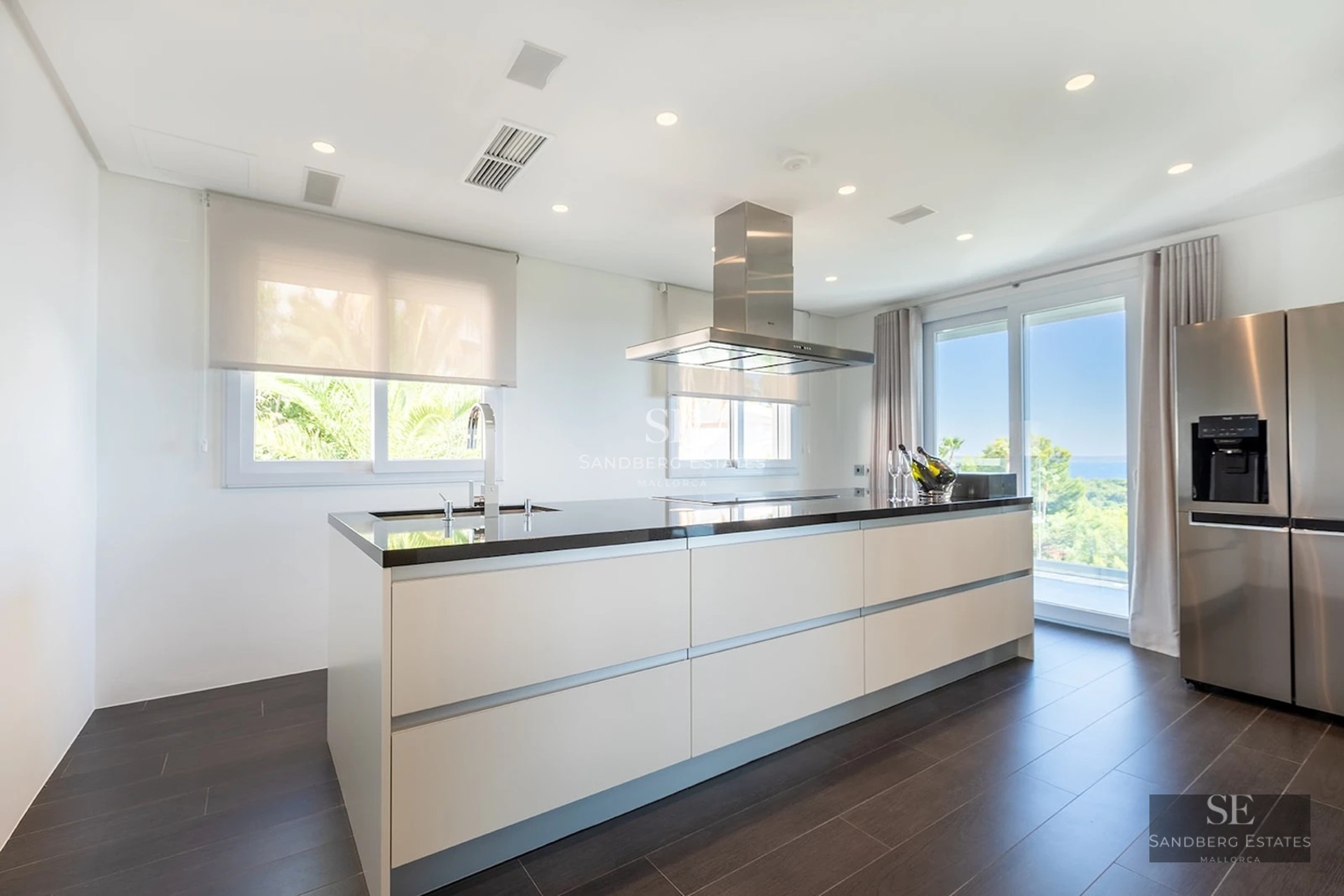 Bright modern kitchen featuring a large white island with black countertop, stainless steel appliances, and sea views.