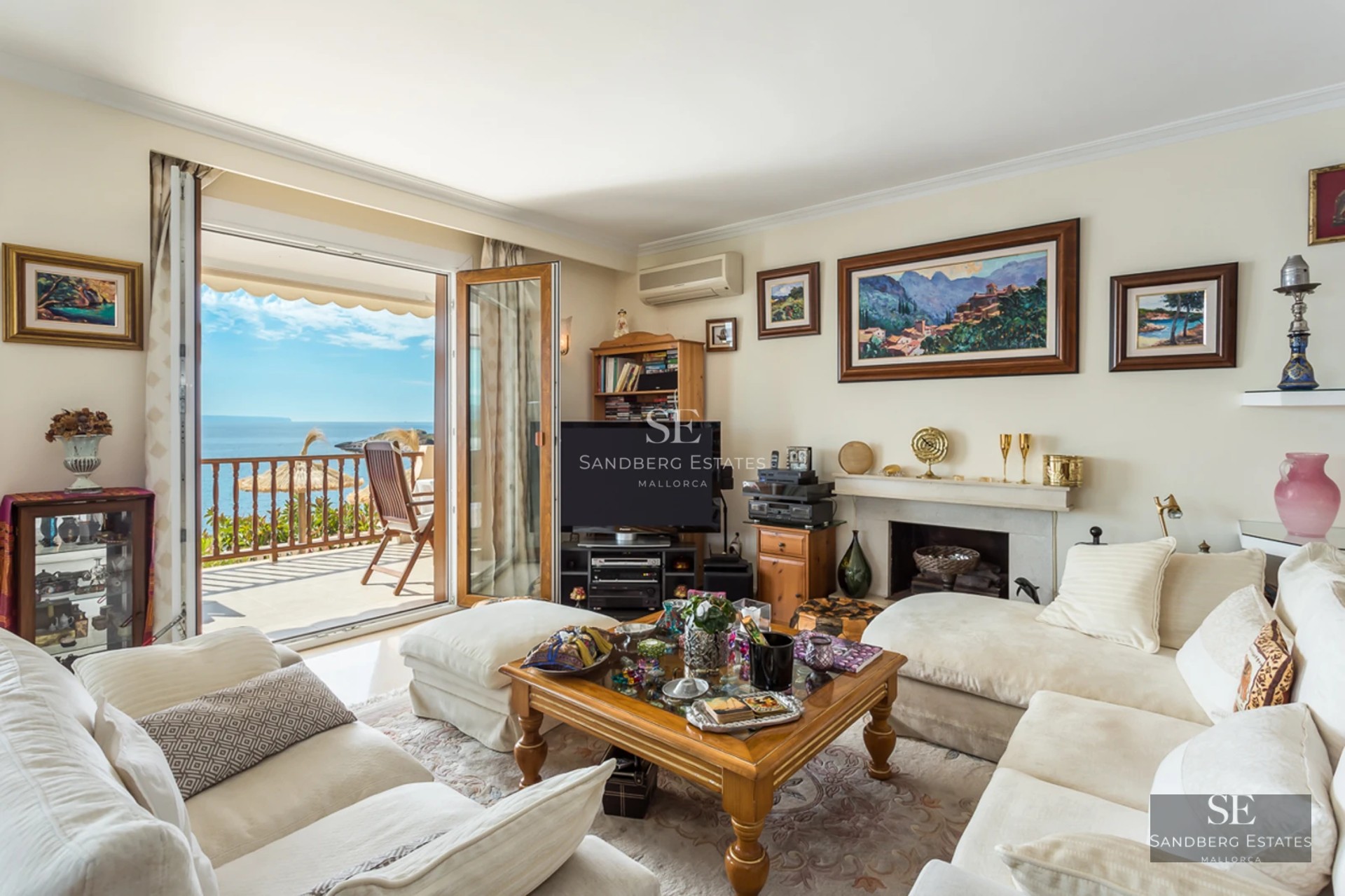 Bright living room with white sofas and a wooden coffee table opening to a terrace with Mediterranean sea views.