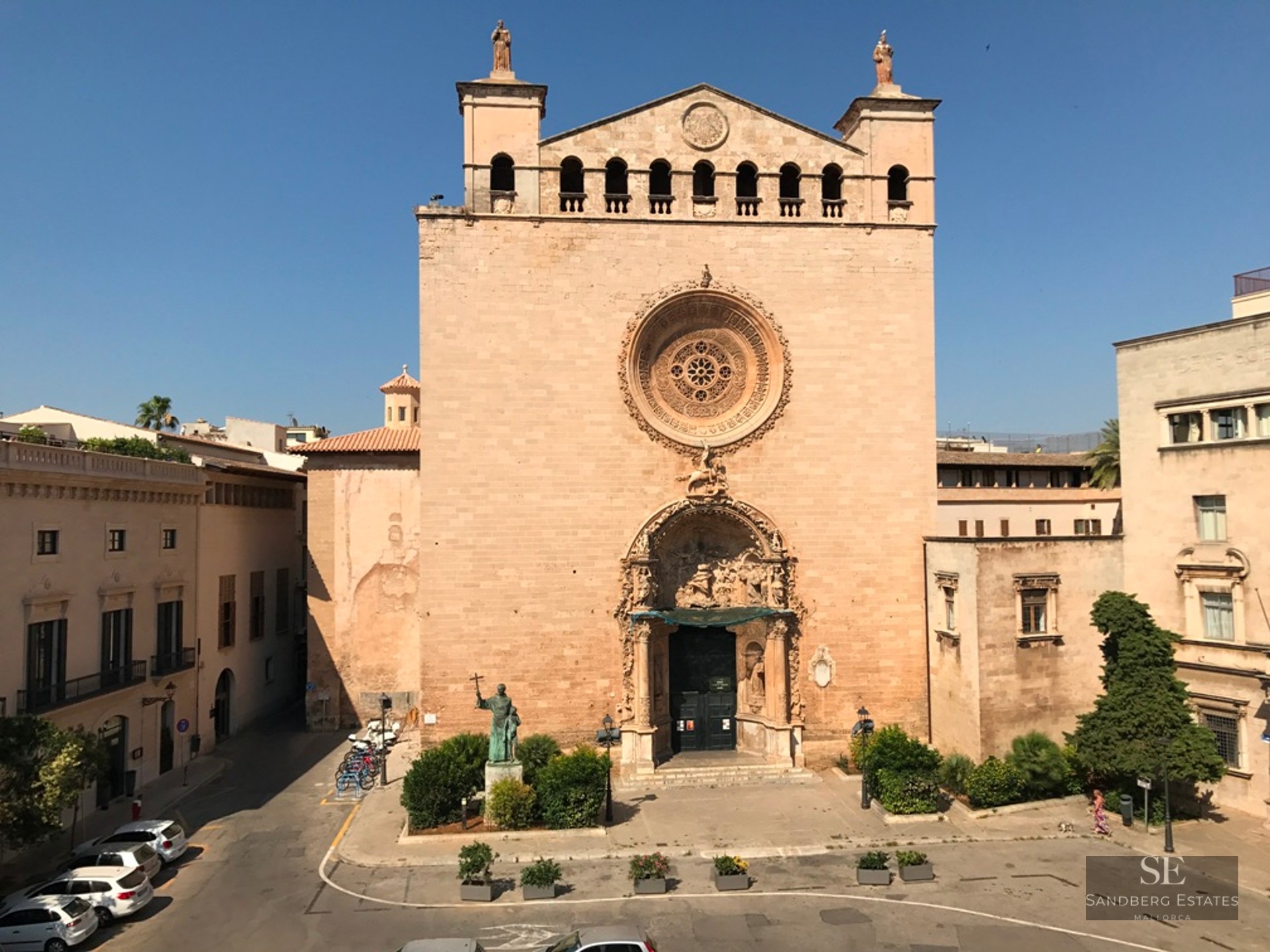 Facade of a historic stone church with a large ornate rose window and a decorative arched entrance on a sunny day.