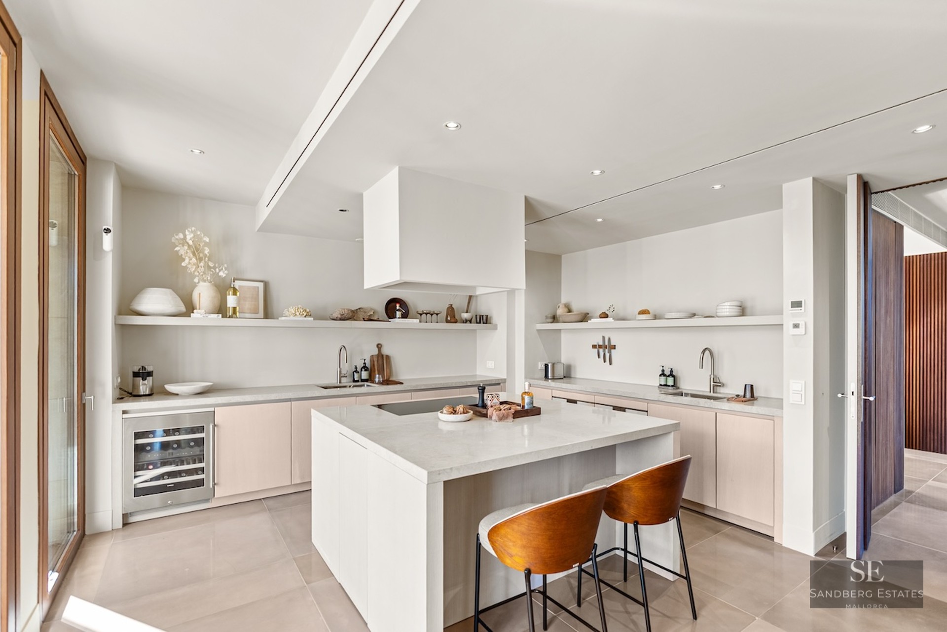 Bright modern kitchen with white island, stone countertops, wine cooler, and warm wood bar stools.