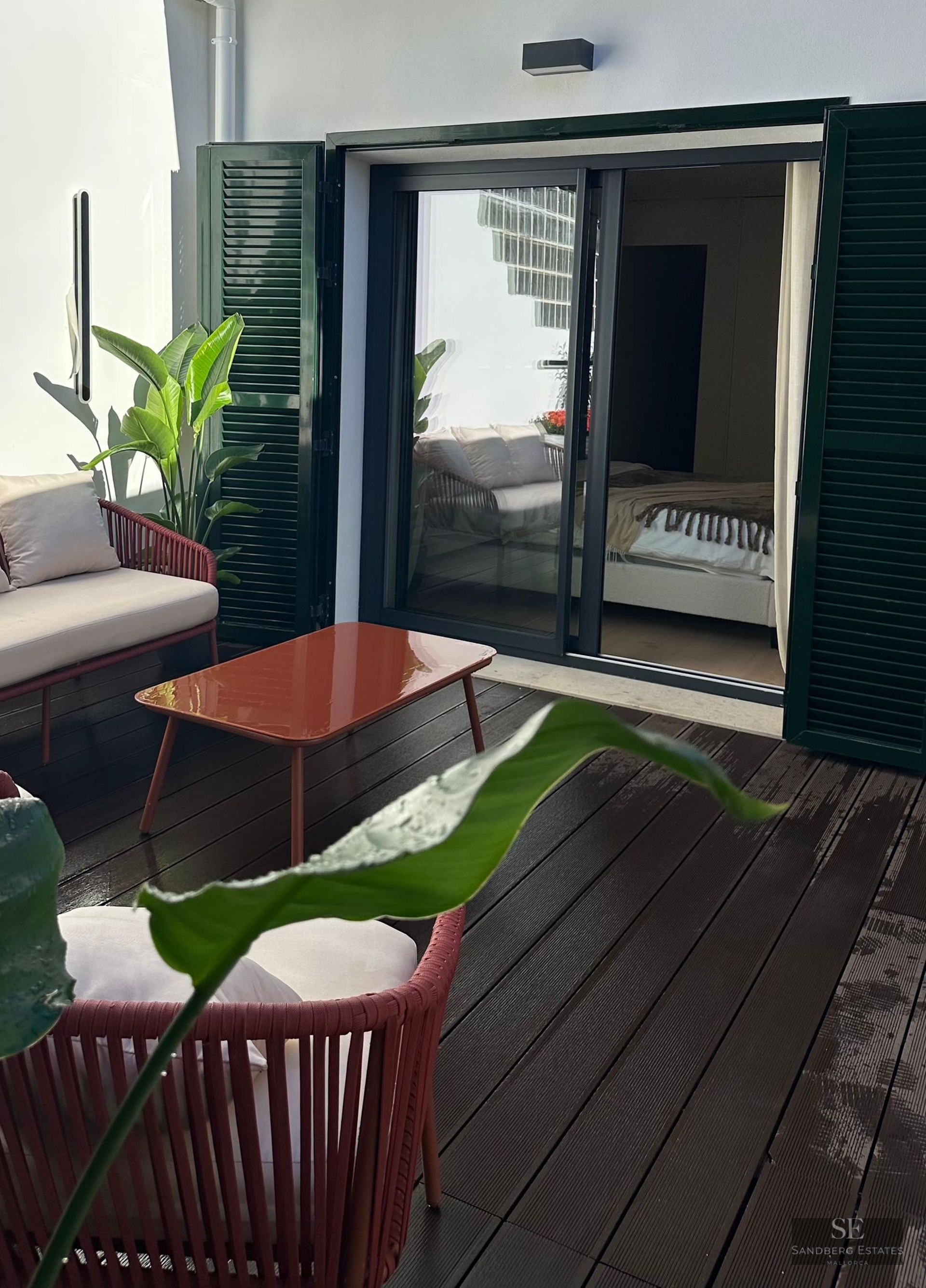 Private outdoor terrace with terracotta furniture, wooden decking, and green shutters next to a bedroom entrance.