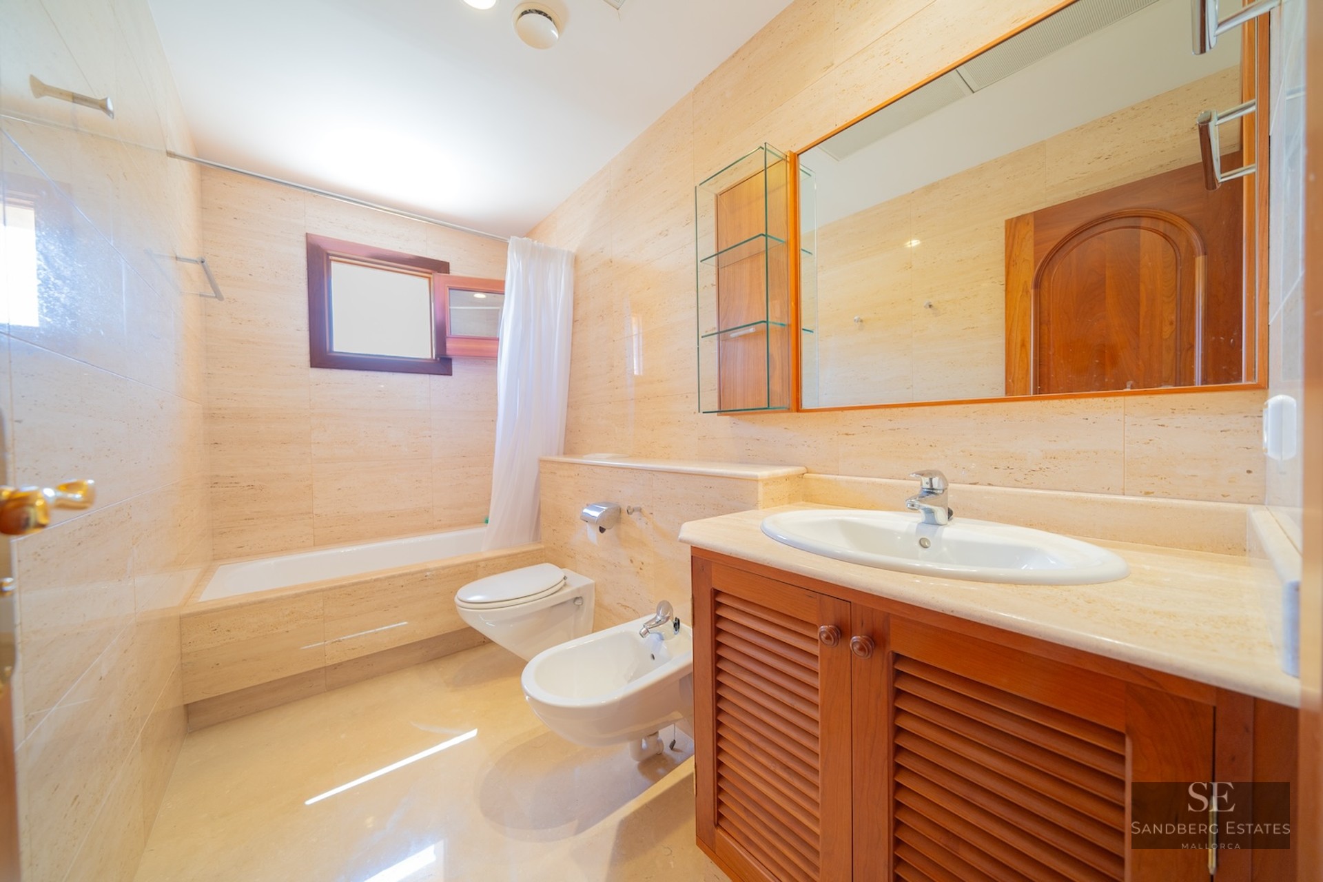 Bathroom featuring beige marble walls, a bathtub, bidet, toilet, and wooden vanity unit.
