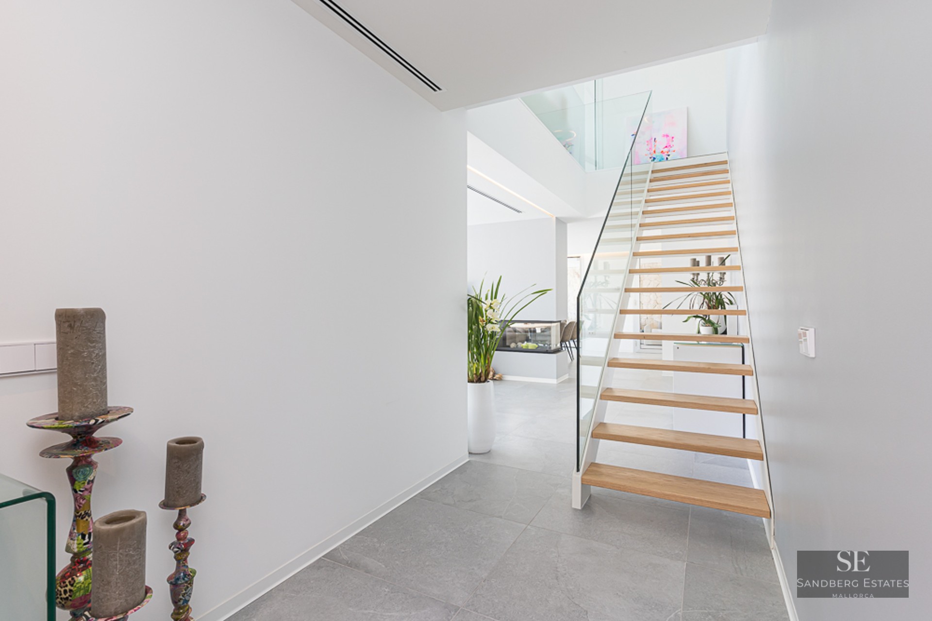 Bright modern hallway featuring a light wood floating staircase with glass railings and grey stone flooring.