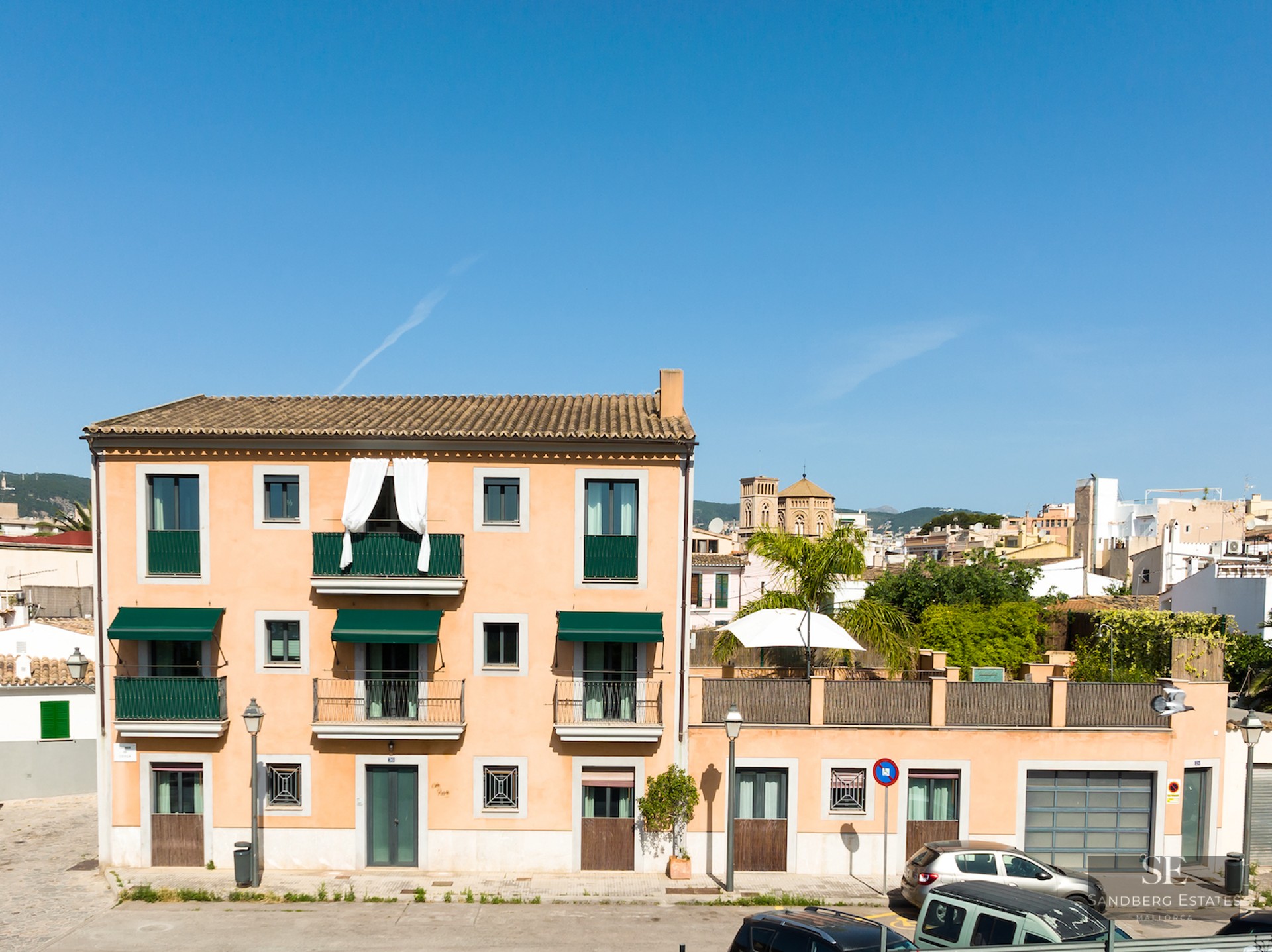 Three-story terracotta building with green balconies and awnings under a clear blue sky.