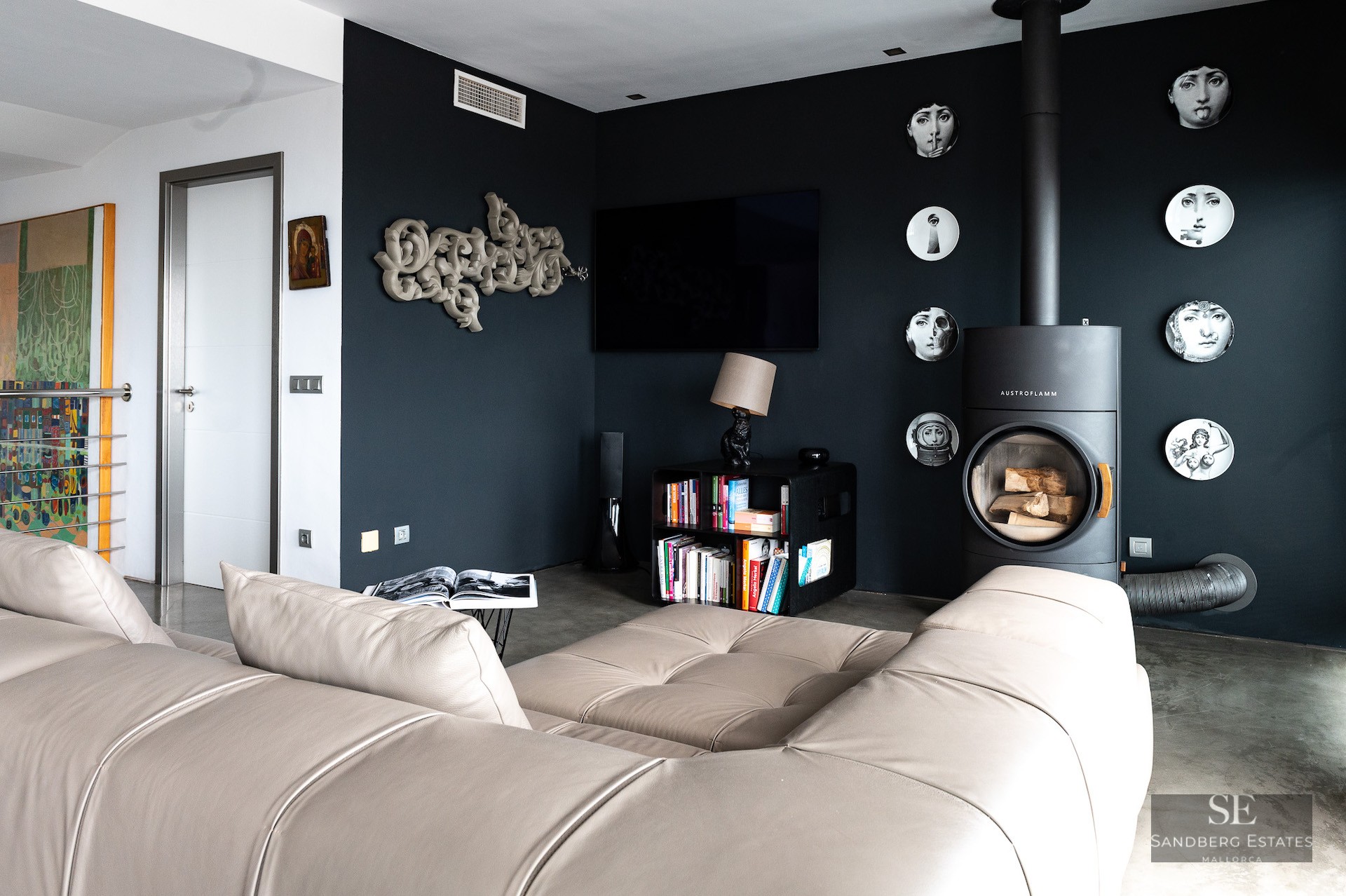 Modern living room with a black accent wall, designer wood-burning stove, leather sofa, and artistic wall decor.