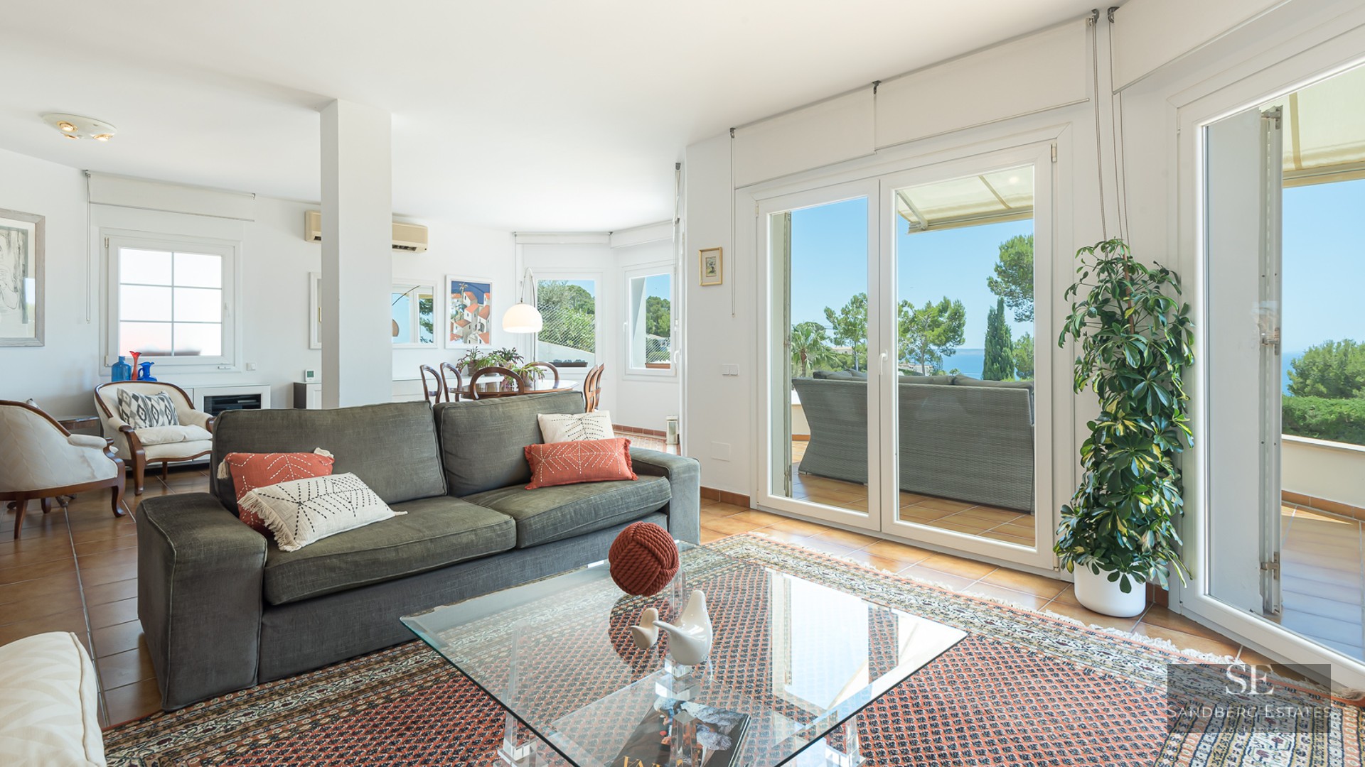 Spacious living room with green sofa, oriental rug, and glass doors opening to a terrace with sea views.