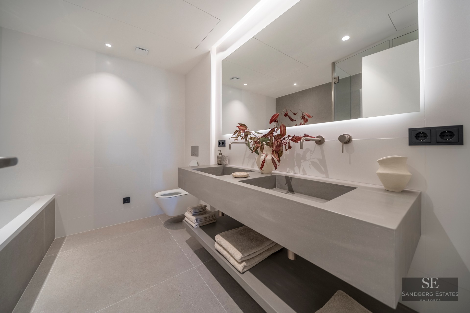 Minimalist bathroom featuring a floating grey concrete double vanity, large backlit mirror, and wall-mounted faucets.