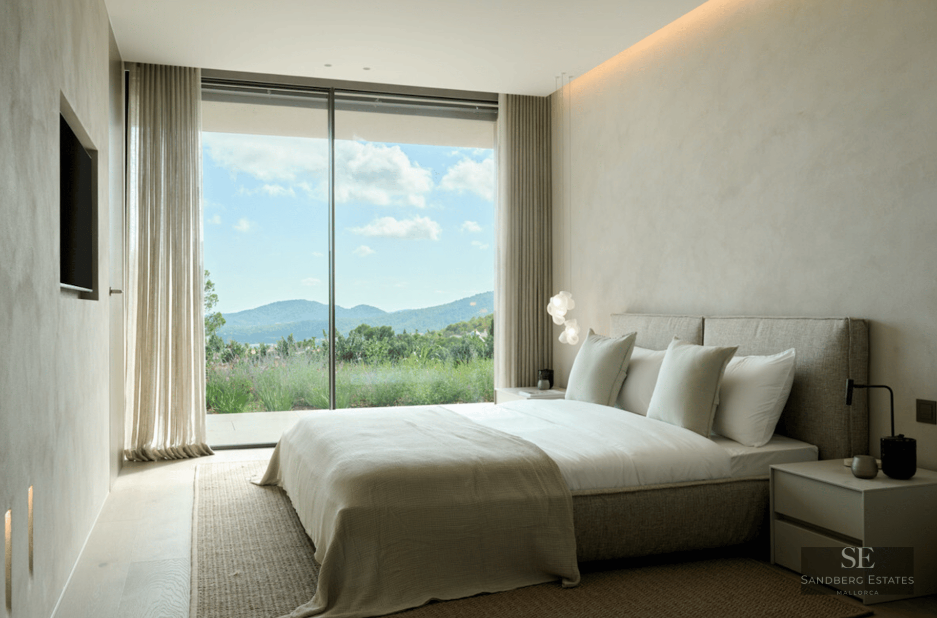 Luxury bedroom featuring textured walls, a minimalist bed, and floor-to-ceiling windows overlooking hills.