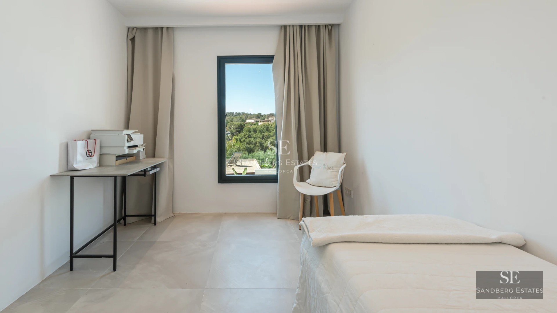 View of an elegant swimming pool surrounded by sun loungers, with a modern villa in the background and lush greenery.