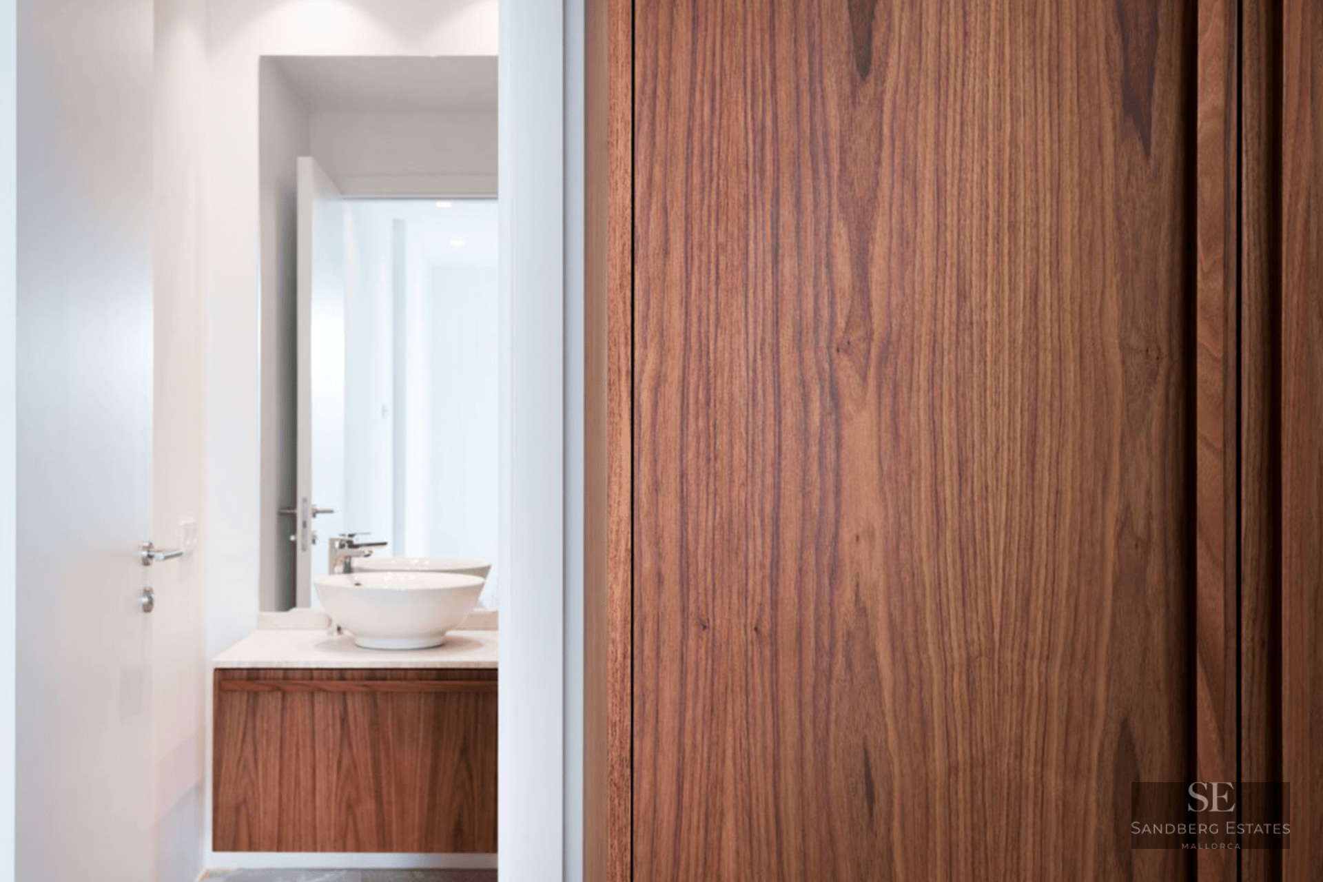 Modern bathroom featuring a white vessel sink on a rich wood floating vanity with a large mirror and bright lighting.