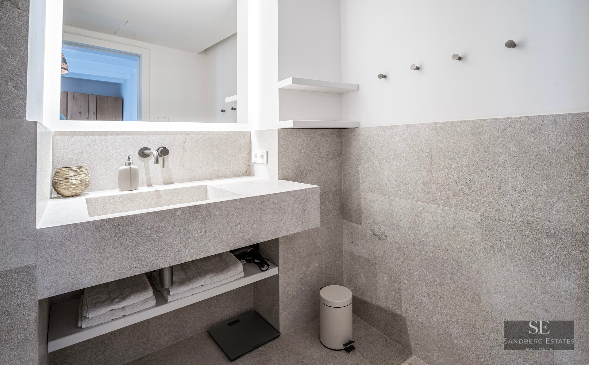 Salle de bain moderne avec vanité flottante en pierre grise, lavabo intégré et grand miroir rétroéclairé.