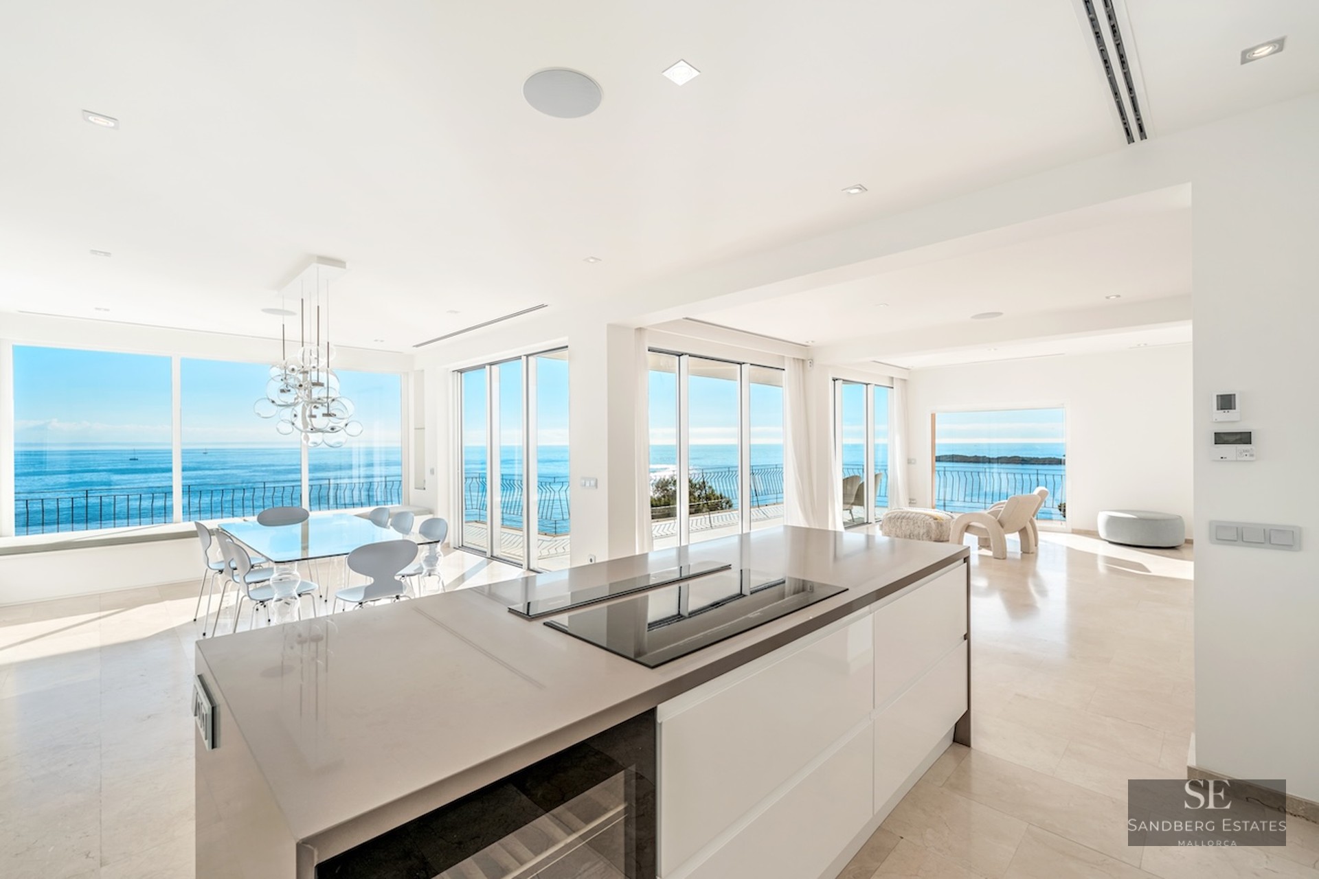 Bright modern kitchen and dining room with large windows showing a wide blue ocean and clear sky.