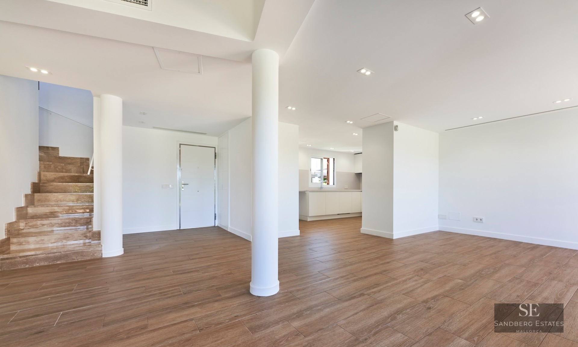 Open plan interior space with wood floors, white pillars, stone stairs, and a white entrance door.