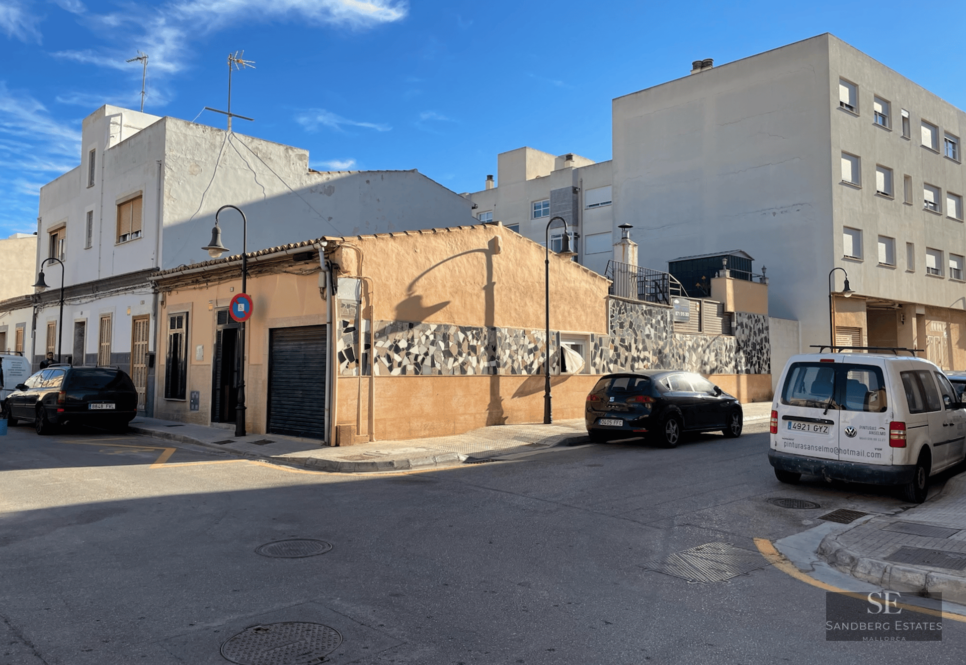 Peach-colored corner building with a mosaic tile strip on a sunny urban street with parked cars and blue sky.