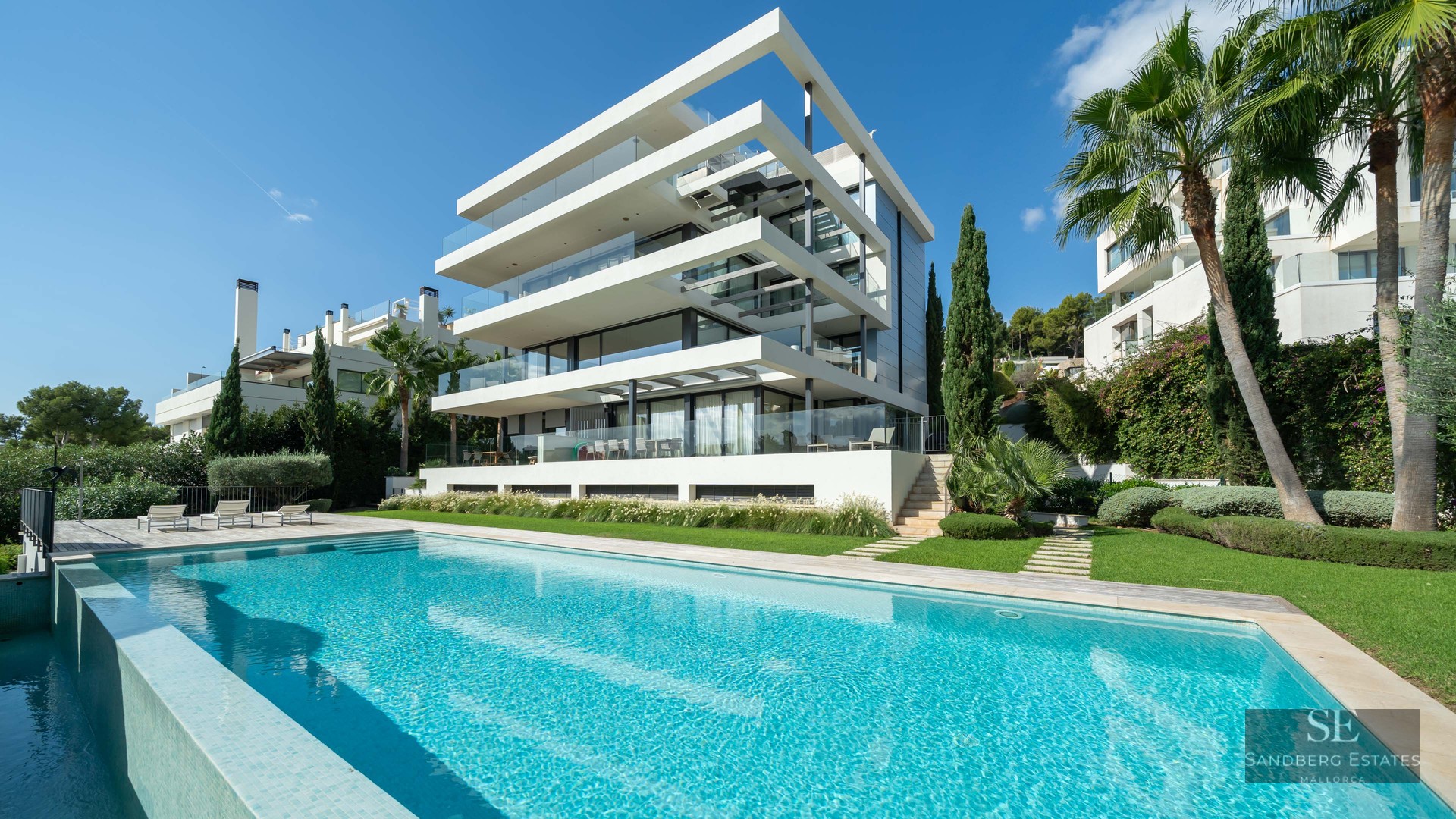 Exterior view of a modern multi-level villa featuring a large turquoise swimming pool and landscaped garden.