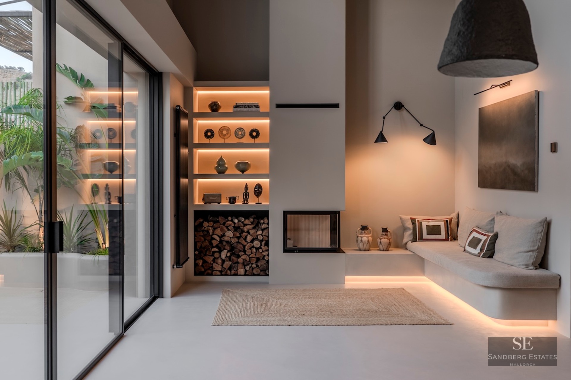 Salon minimaliste moderne avec canapé intégré, éclairage encastré, cheminée et grandes baies vitrées coulissantes.