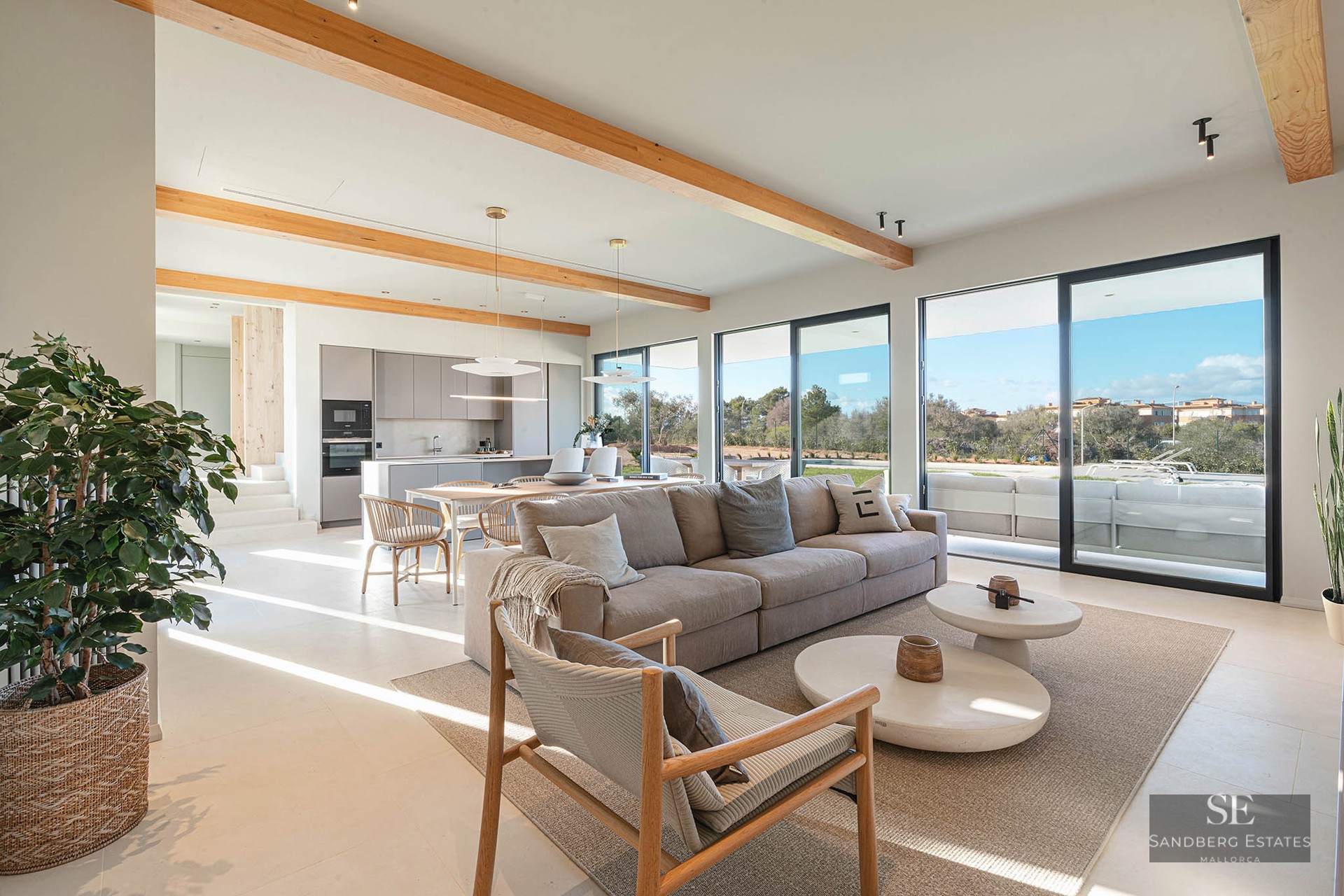 Spacious modern living room with large beige sofa, wooden ceiling beams, and floor-to-ceiling glass doors.