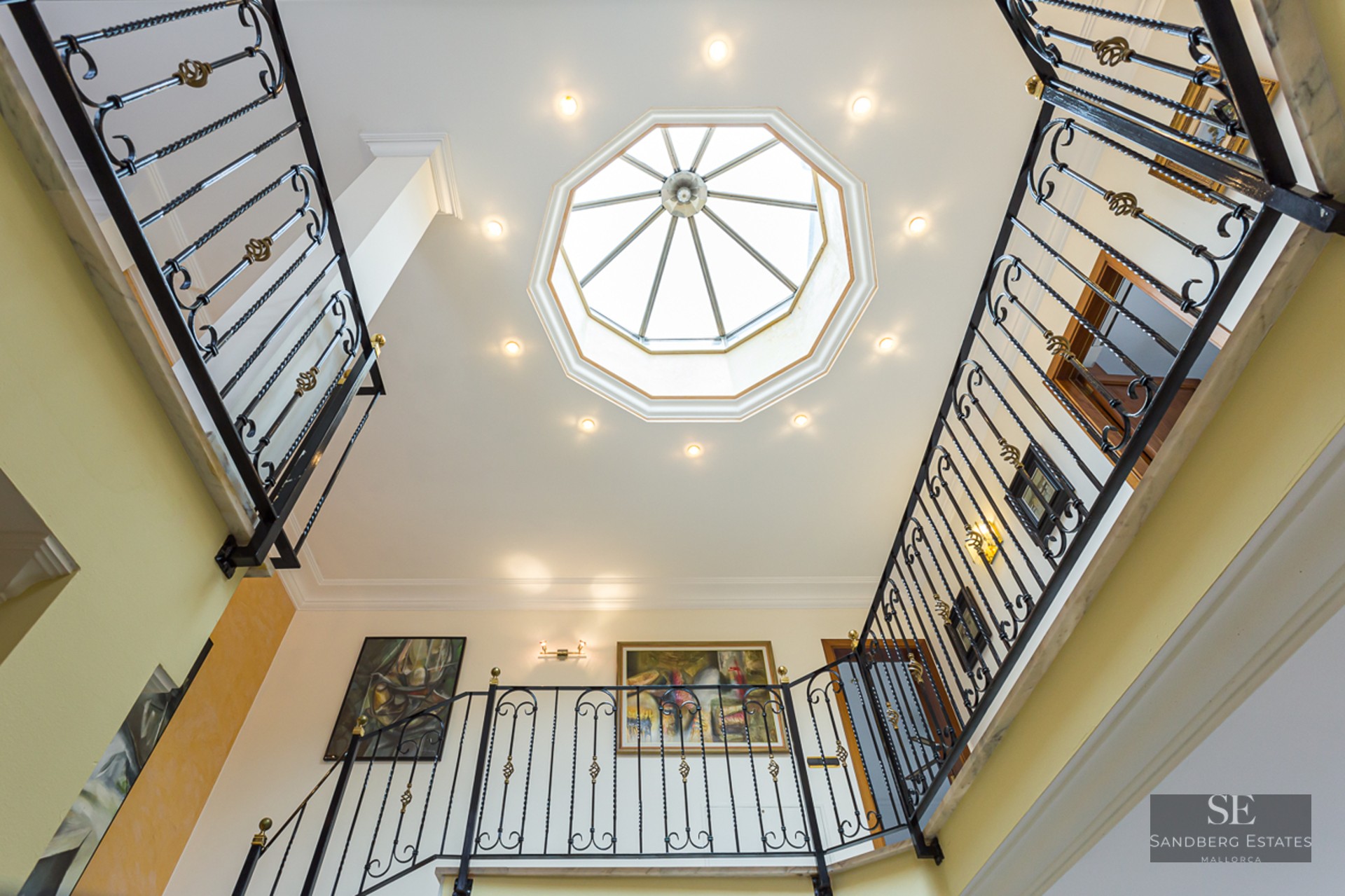 Upward view of a grand staircase with wrought iron railings and a large octagonal skylight in the ceiling.