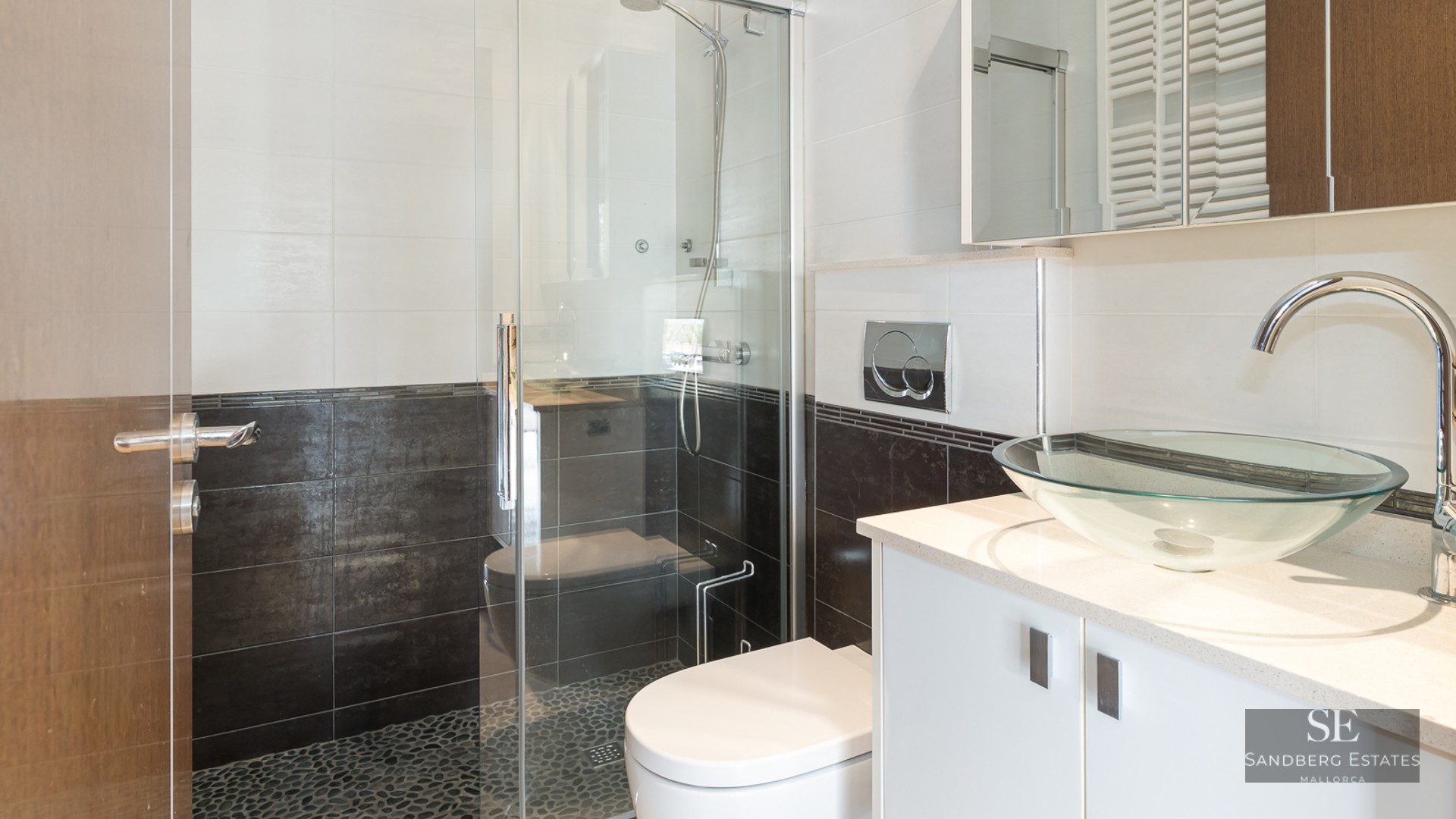 Modern bathroom featuring a glass bowl sink, white vanity, and a glass-enclosed shower with pebble tile floor.