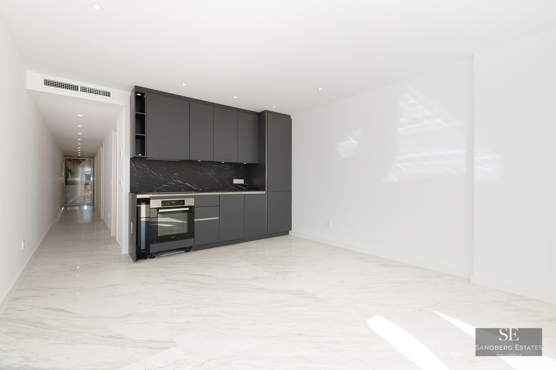 Modern kitchen area with dark gray cabinets, black marble backsplash, and white marble floors in a bright open room.