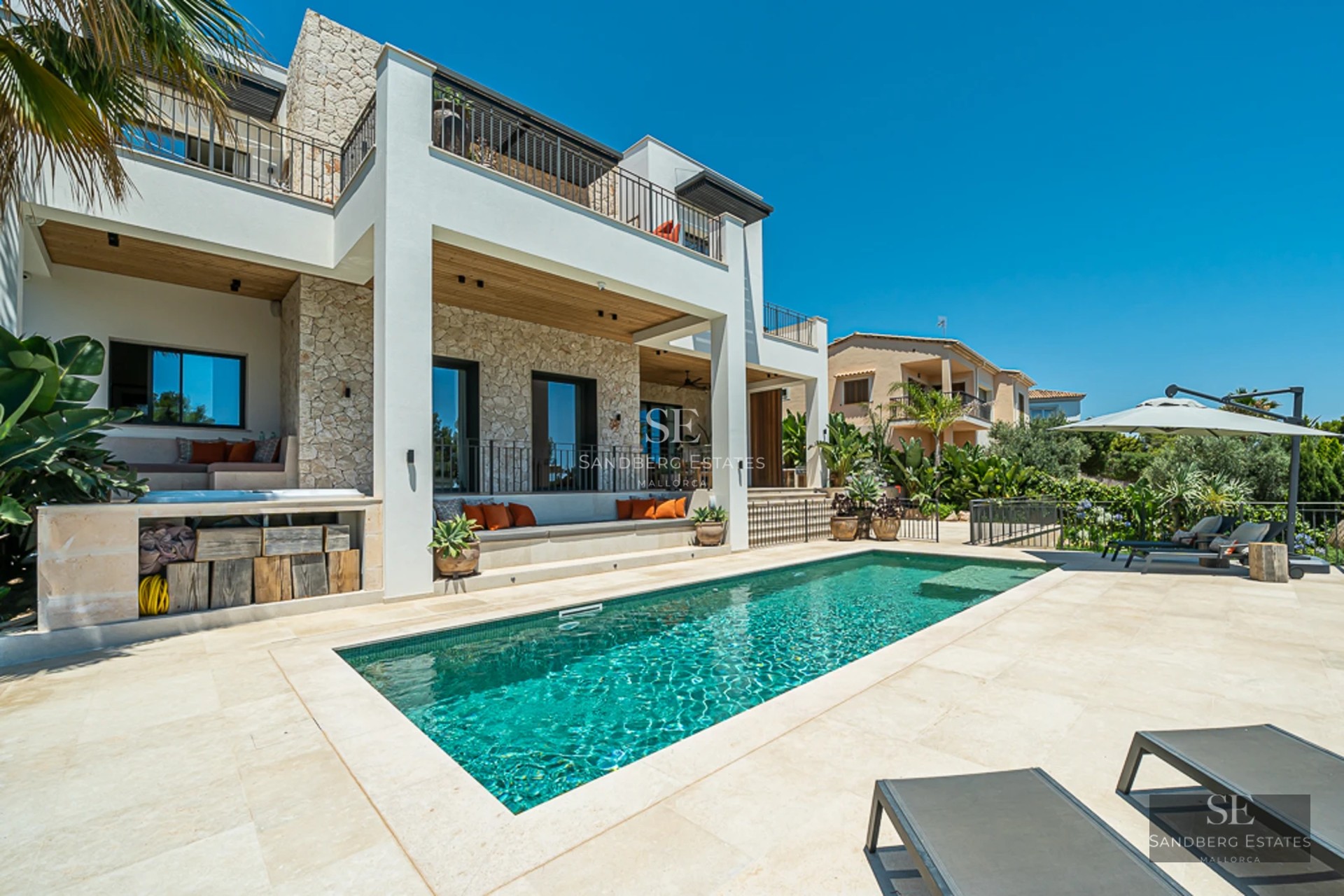 Vue extérieure d'une villa moderne avec piscine, pelouse soignée et grandes fenêtres réfléchissant la lumière du soleil.